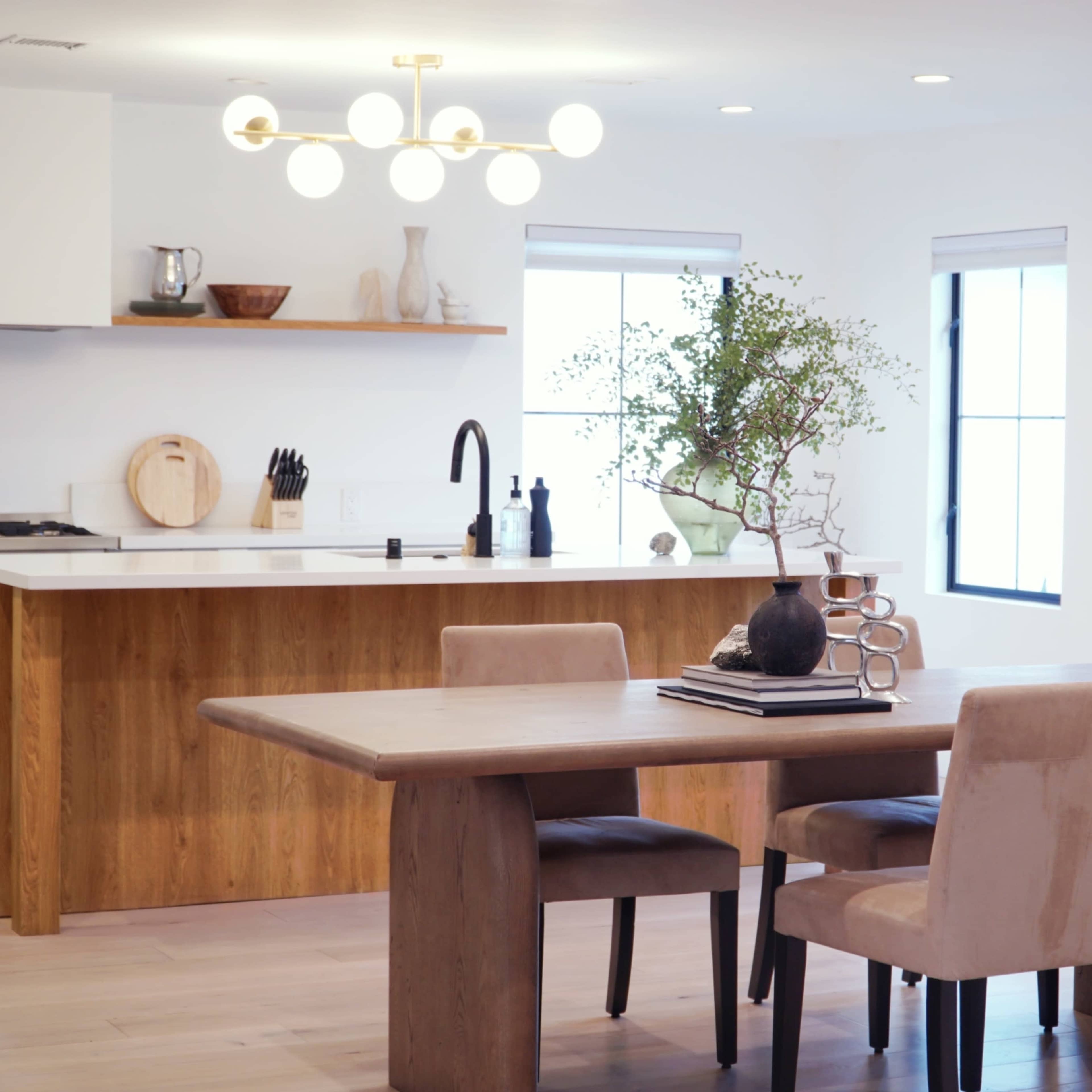 A dining area features a wooden table surrounded by four chairs, with a modern kitchen visible in the background.