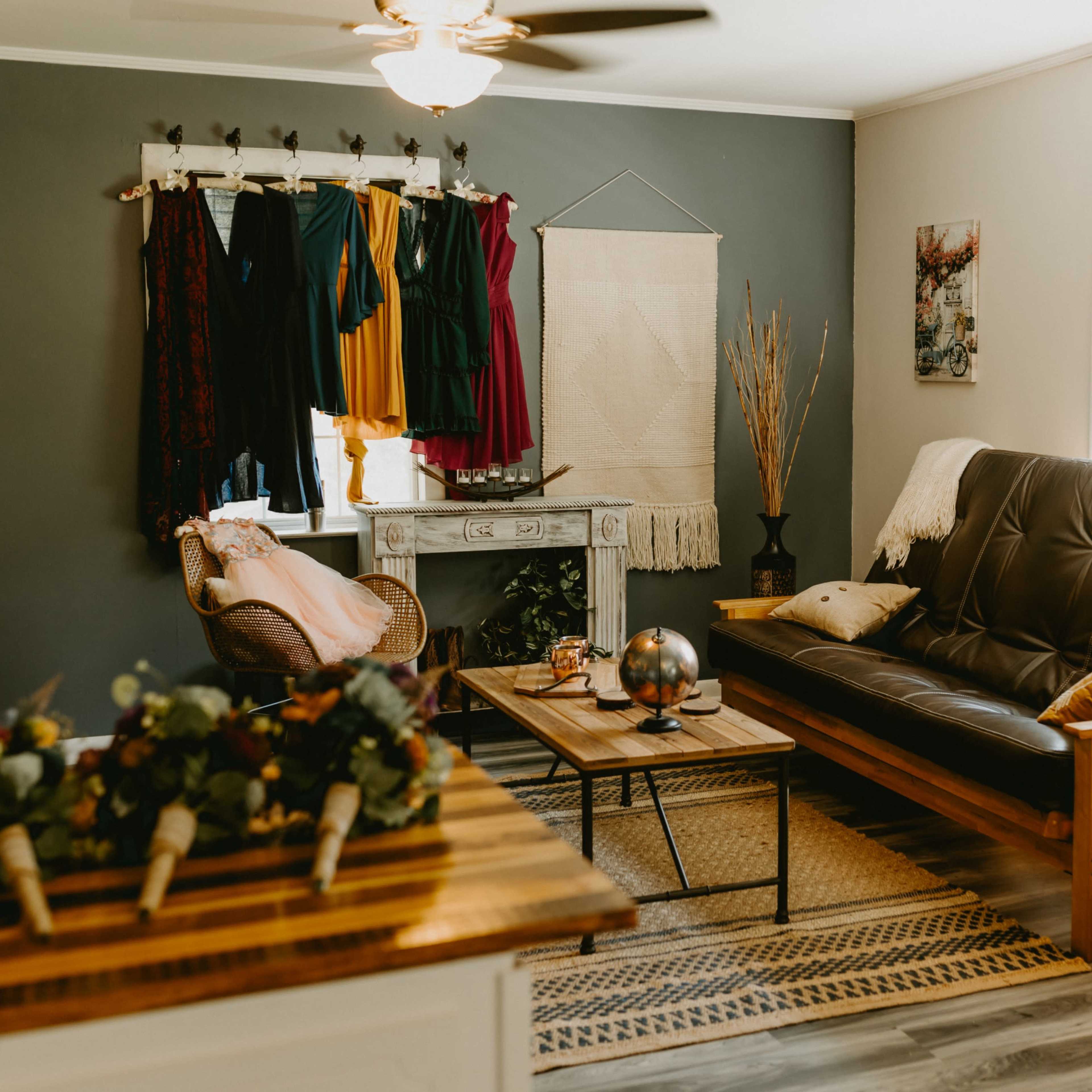 The scene depicts a cozy living room featuring a dark sofa, a wooden coffee table, and a rack displaying colorful dresses on the wall.