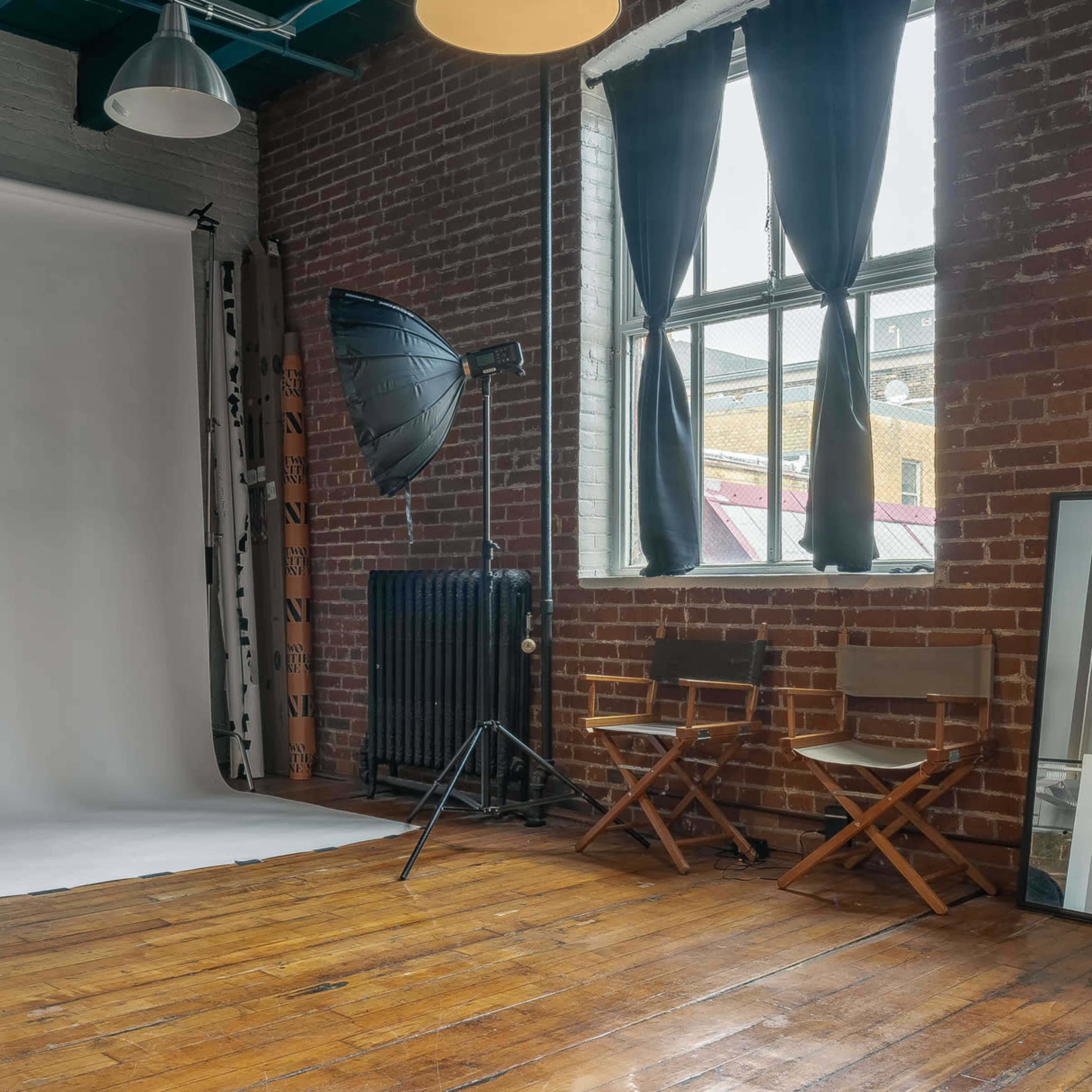 A photography studio features two large softbox lights, a backdrop, and two chairs positioned near a window with industrial-style elements.