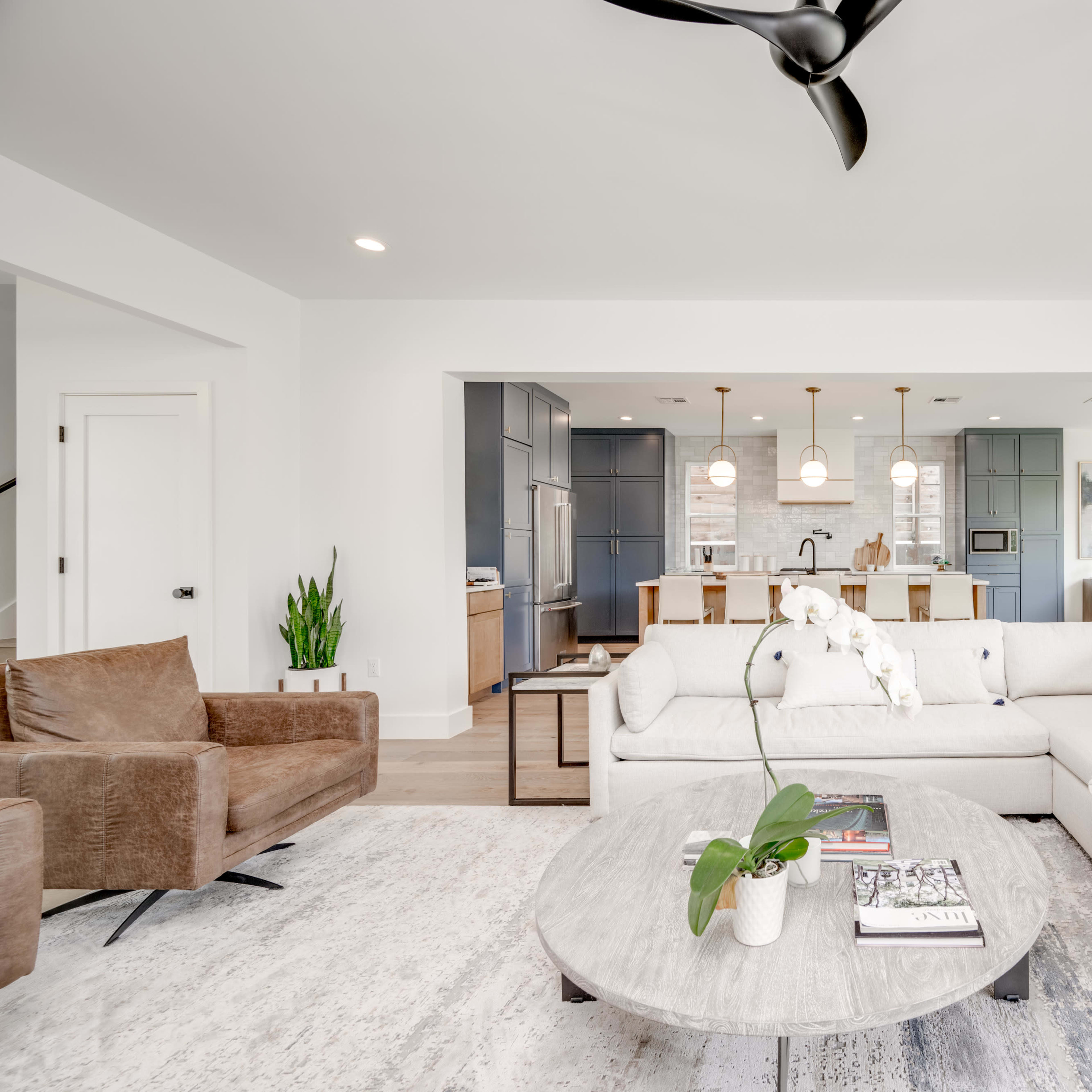 A modern living room featuring a sectional sofa, coffee table, and open access to a kitchen in the background.
