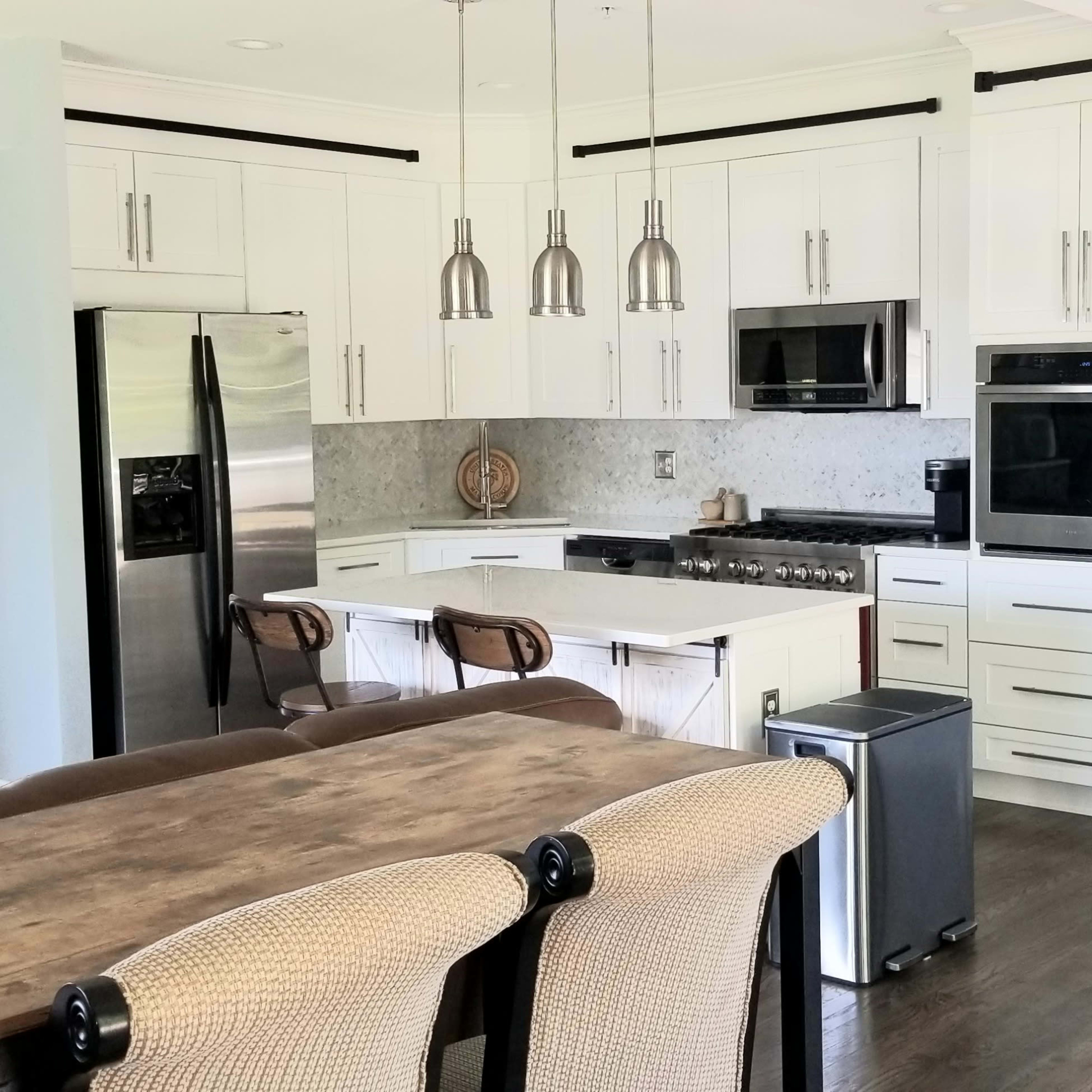 A modern kitchen with white cabinets, stainless steel appliances, and a wooden dining table with upholstered chairs.