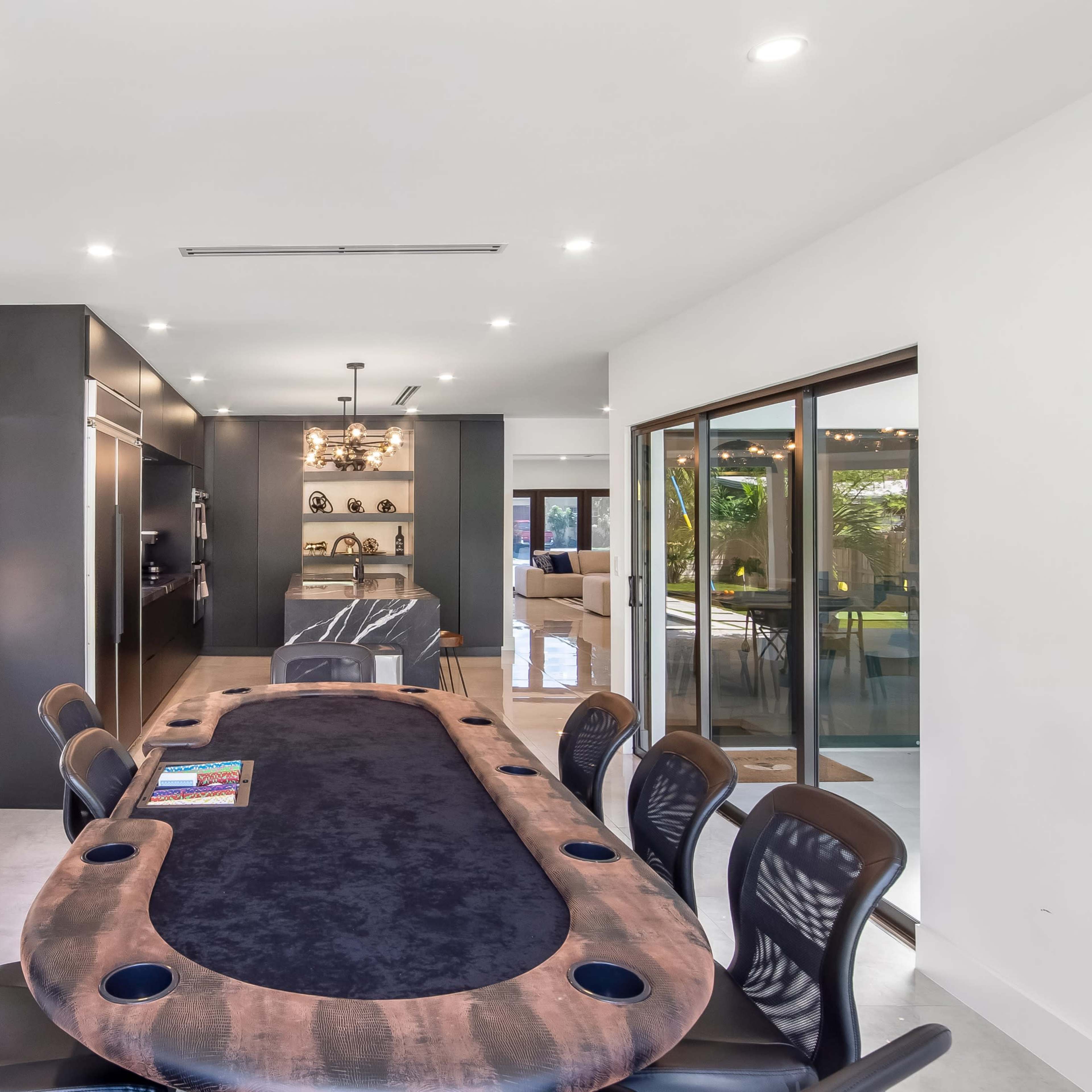 A modern dining area featuring a large, dark table surrounded by black chairs, with a wall-mounted TV and an open view into a living space.