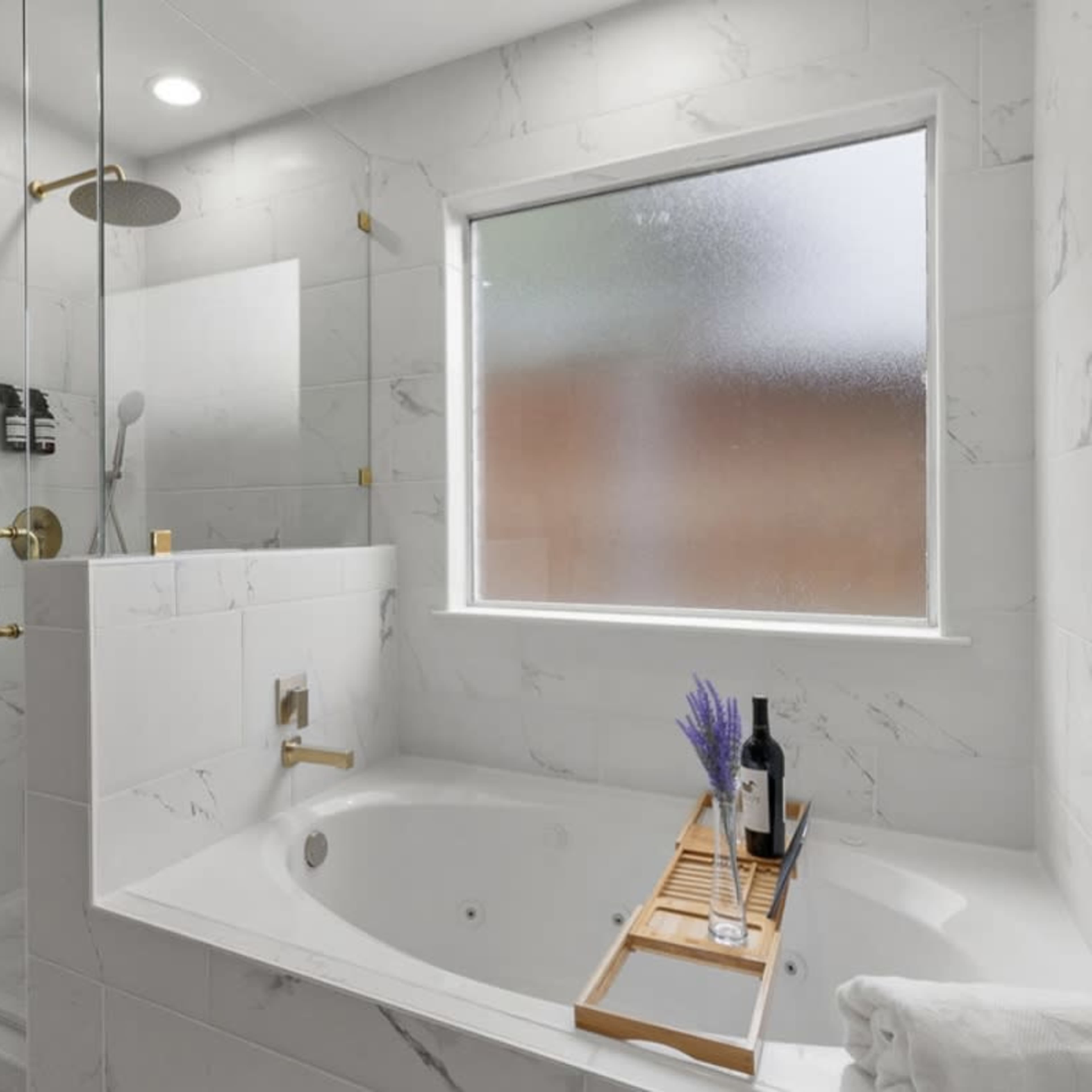 A bathroom with a glass shower enclosure, a large bathtub, and a window allowing natural light in.