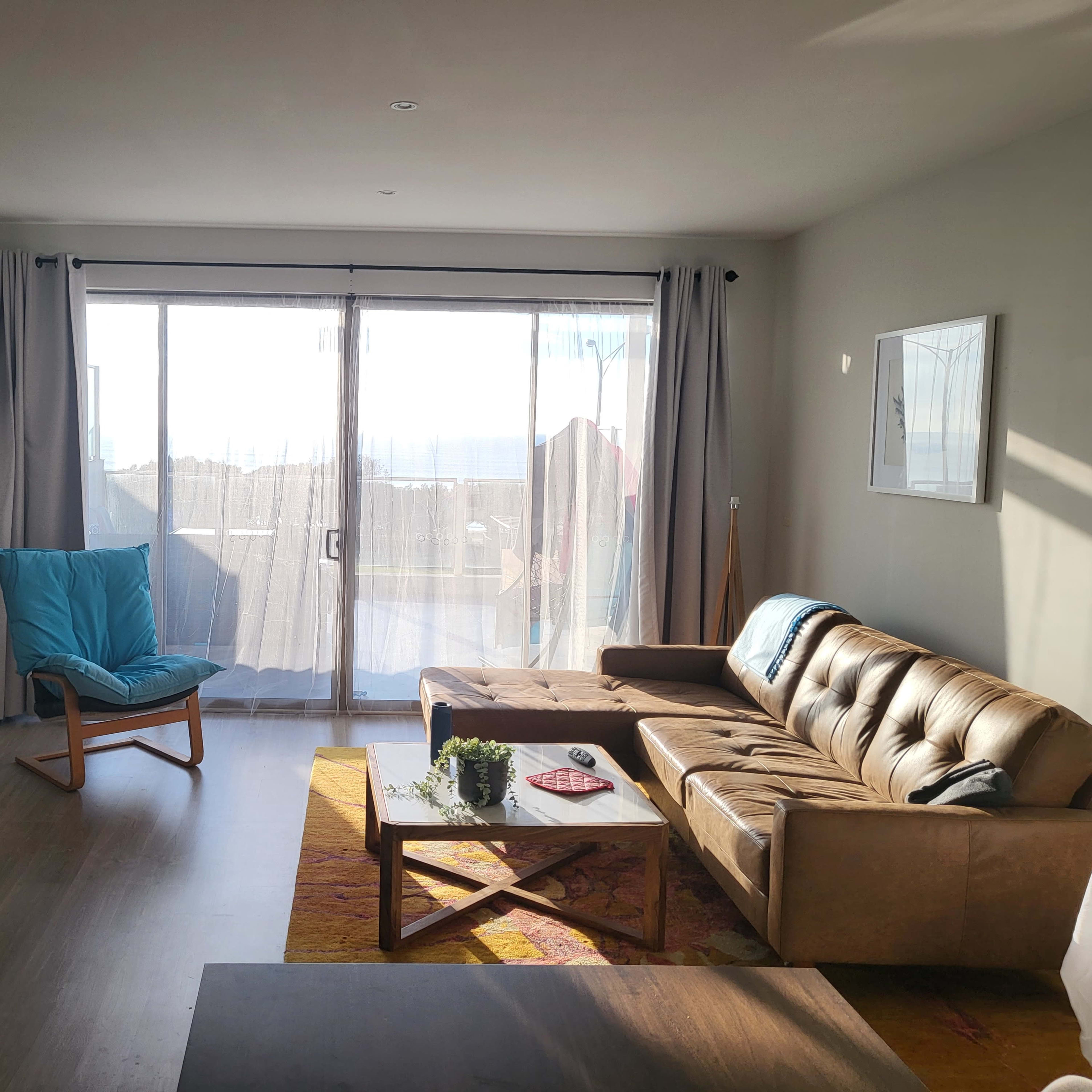 A living room features a brown sofa, a wooden coffee table, a blue chair, and large sliding glass doors leading to an outdoor area.