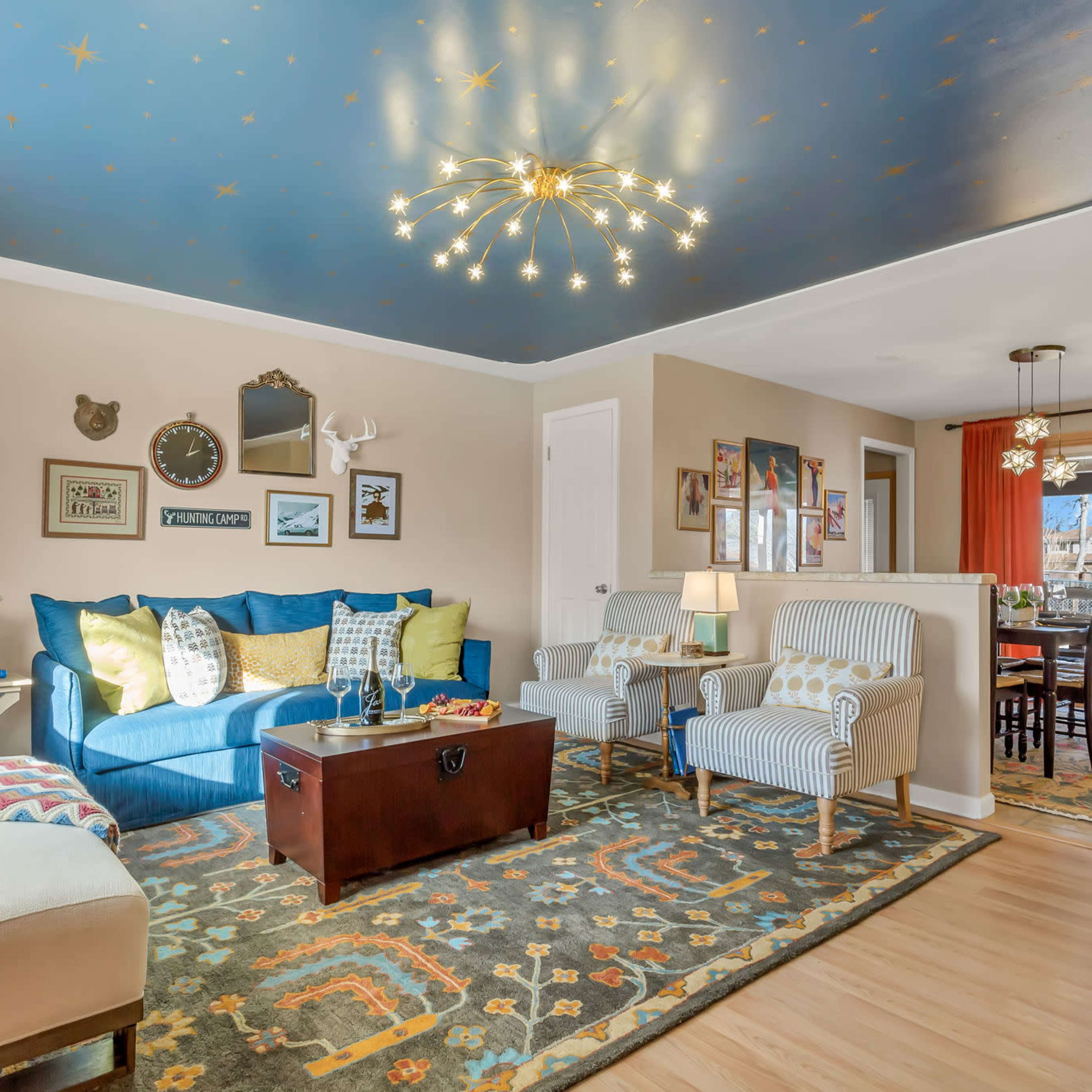 The living room features a blue sofa, patterned area rug, a wooden coffee table, and a dining area with a view through sliding glass doors.