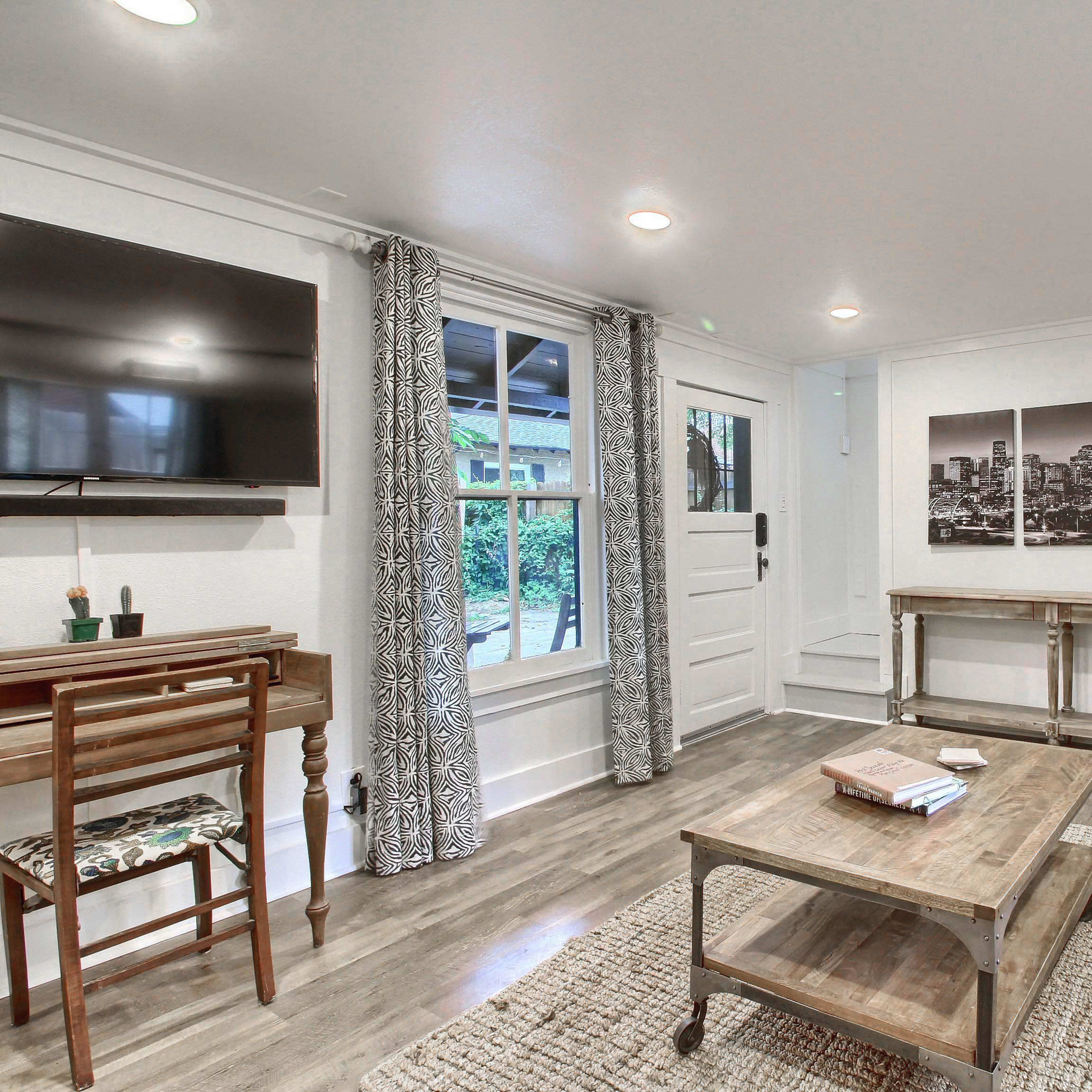 A modern living room with a television, a small wooden table, a couch, and large windows letting in natural light.