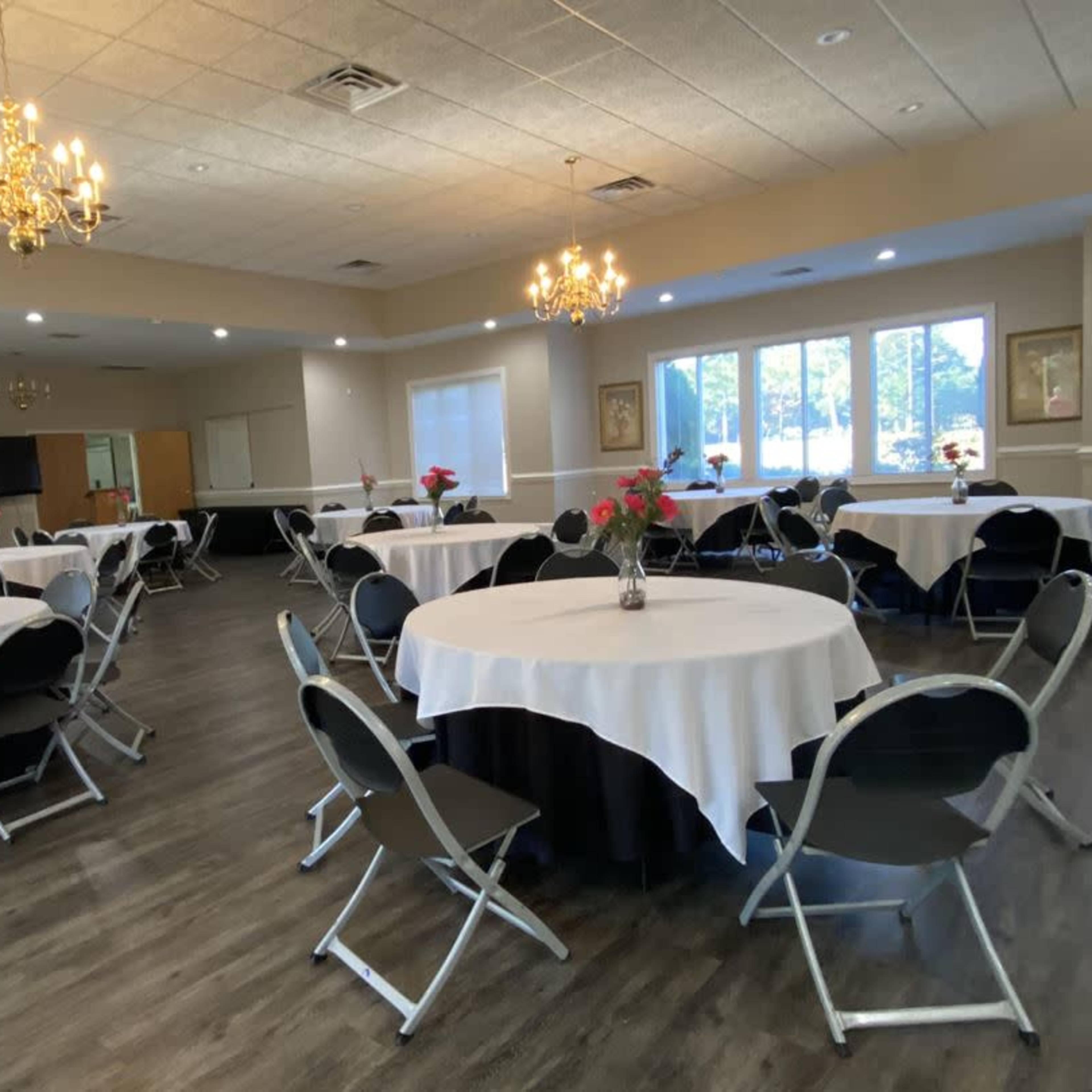 A banquet hall set up with circular tables covered in white tablecloths and chairs arranged around them, with chandeliers hanging from the ceiling.