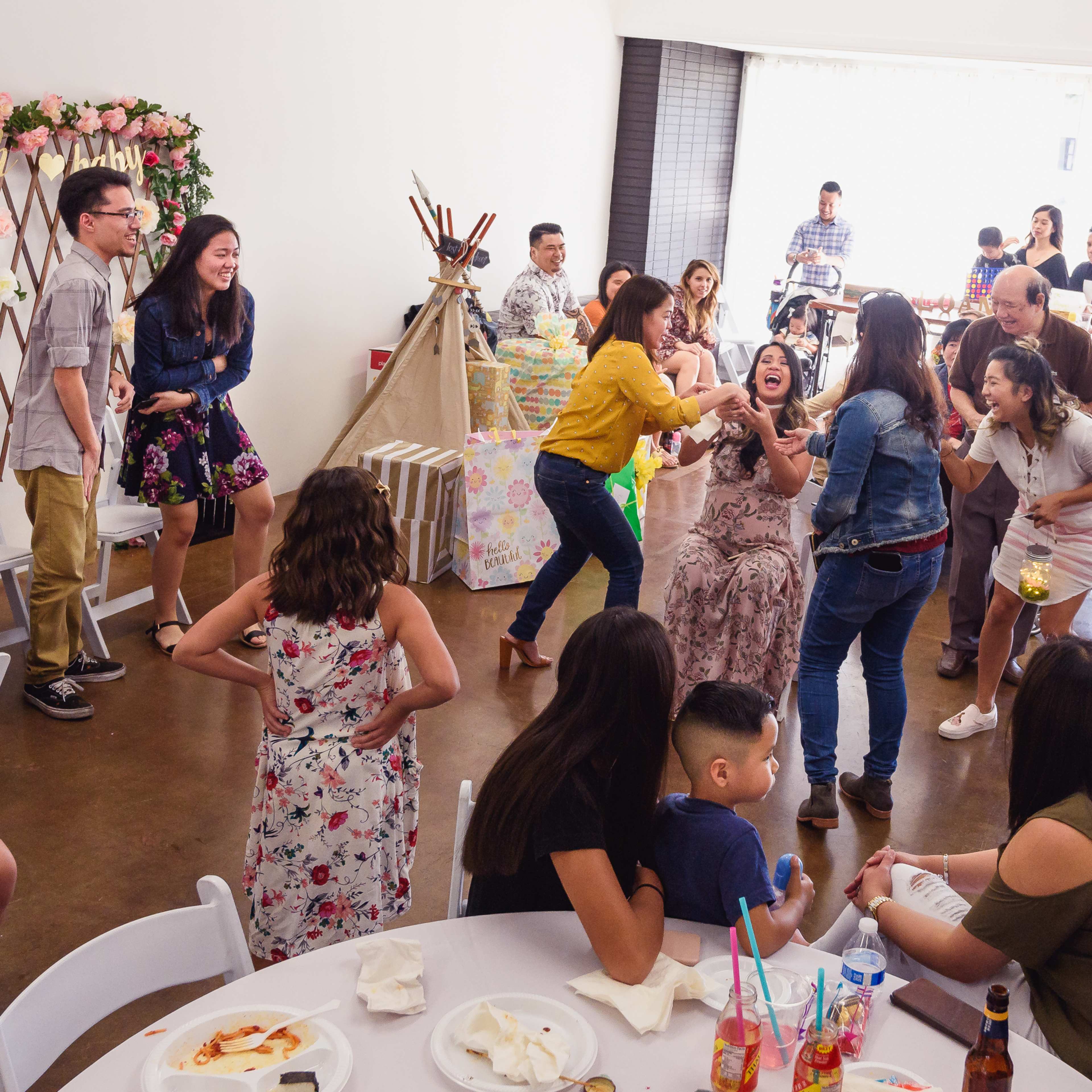 A lively gathering takes place in a decorated indoor space, with guests interacting and enjoying food and drinks at tables.
