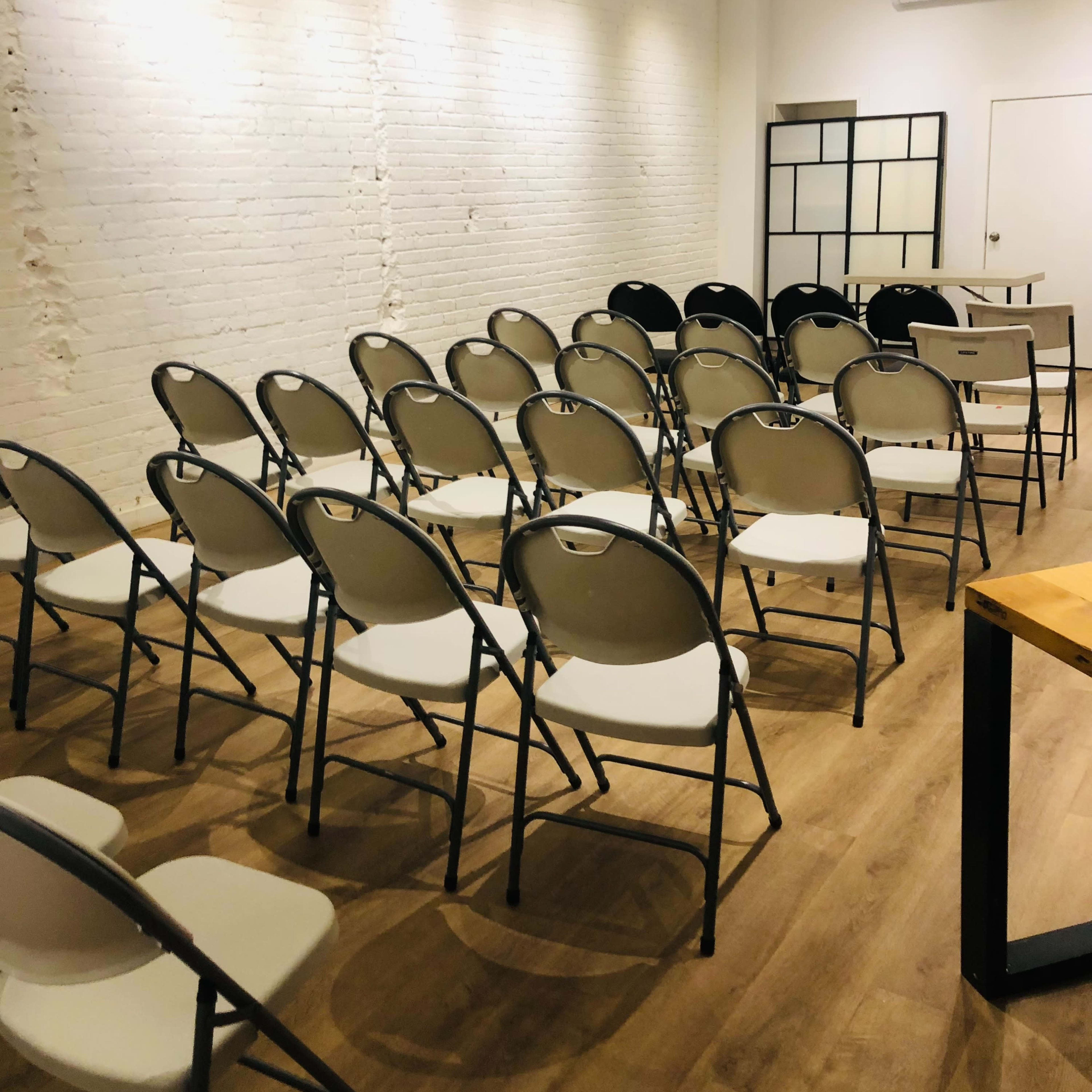 A room with white brick walls and a row of neatly arranged folding chairs facing a blank wall.