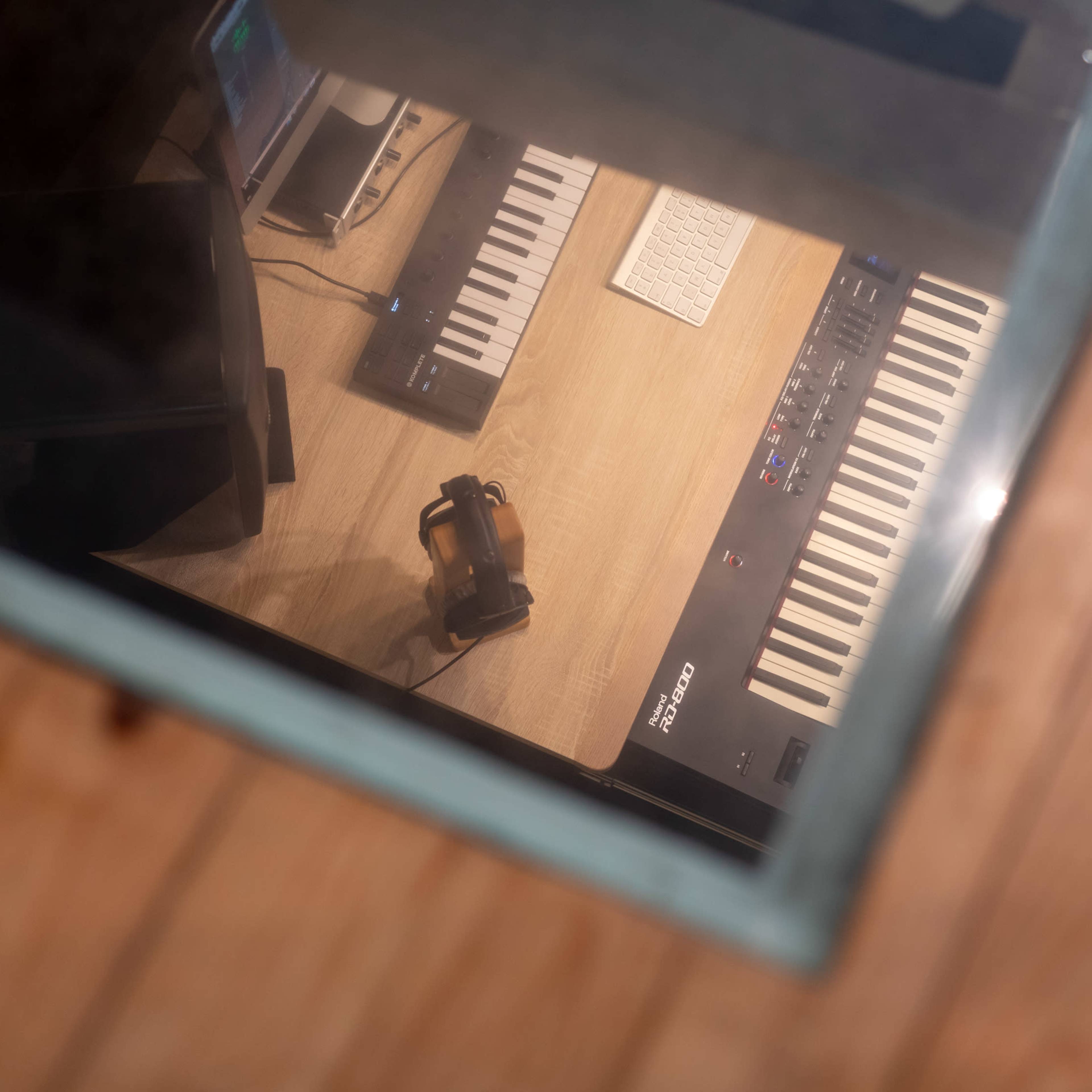 A wooden workspace with two keyboards, a computer monitor, a computer keyboard, and a microphone.