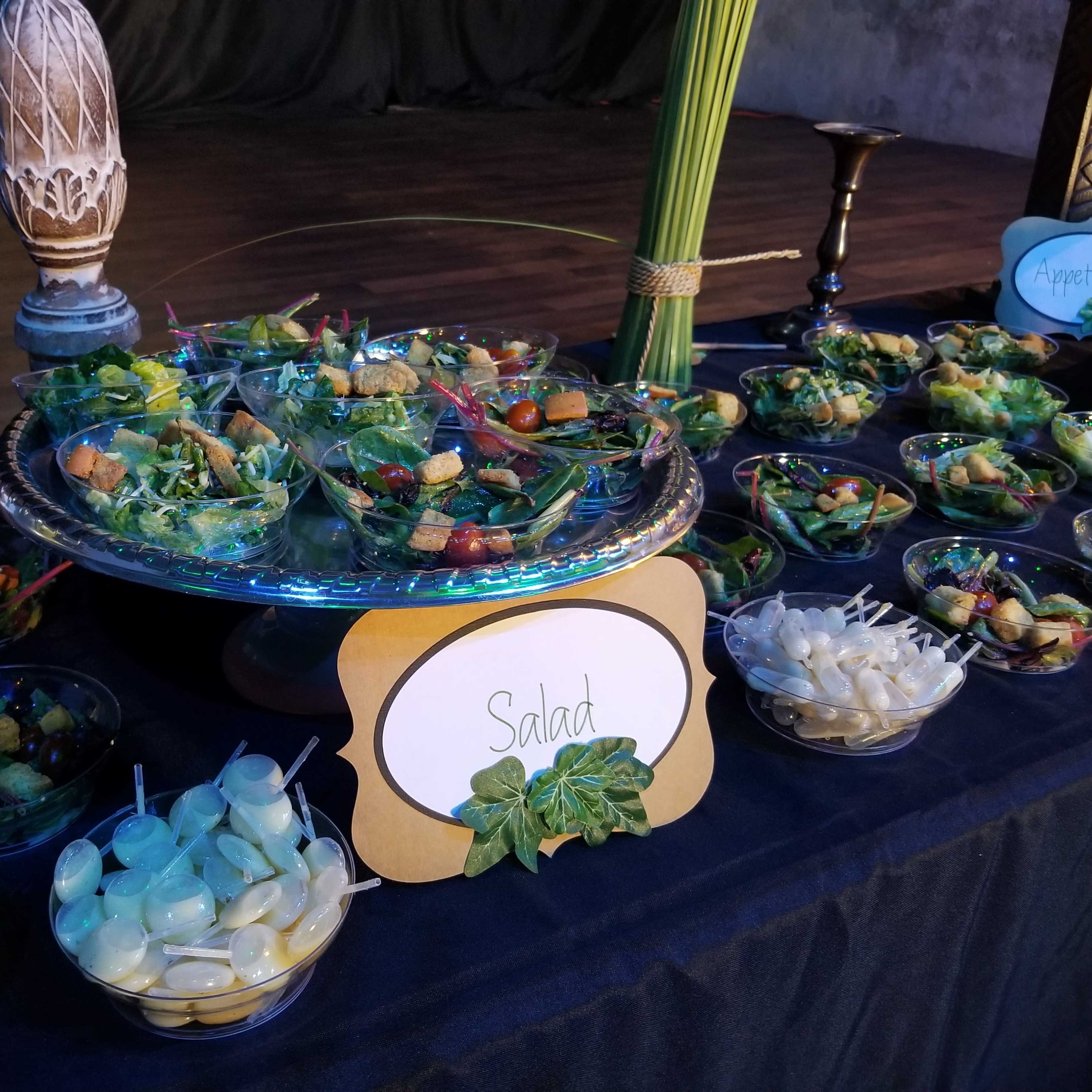 A table is set with various bowls of salads, appetizers, and garnishes, arranged attractively for an event.