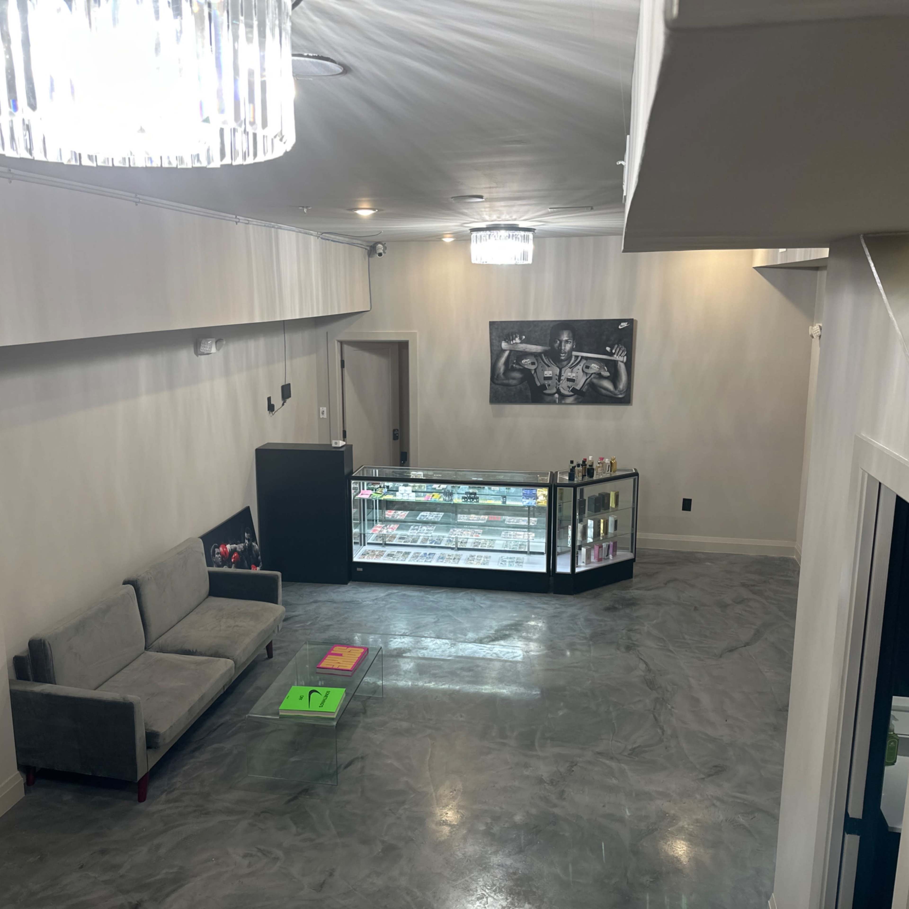 A spacious interior of a modern retail space featuring a gray sofa, an illuminated display case, and artistic wall decor under a chandelier.