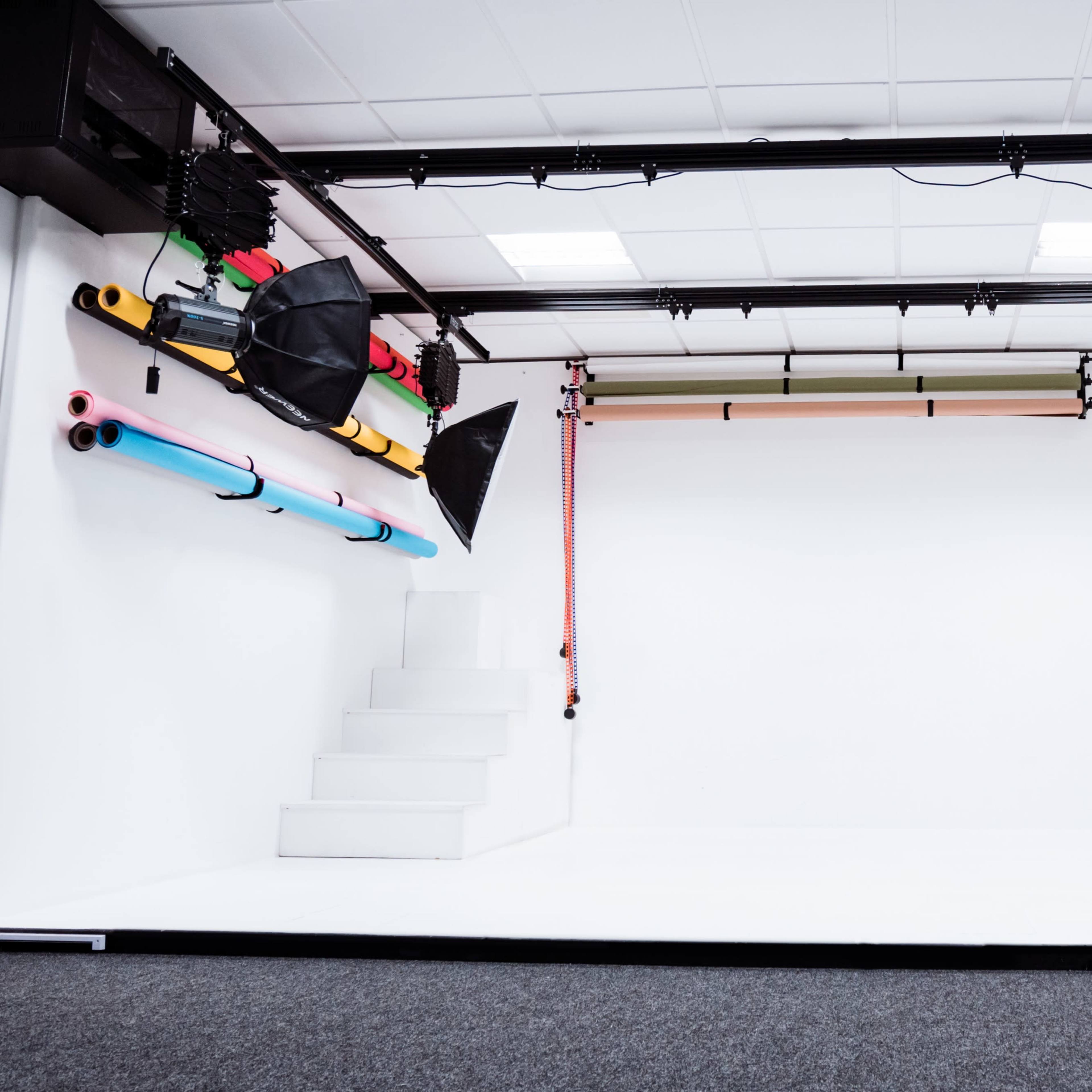 A photography studio with a white backdrop, lighting equipment, and colorful backdrops on the wall.