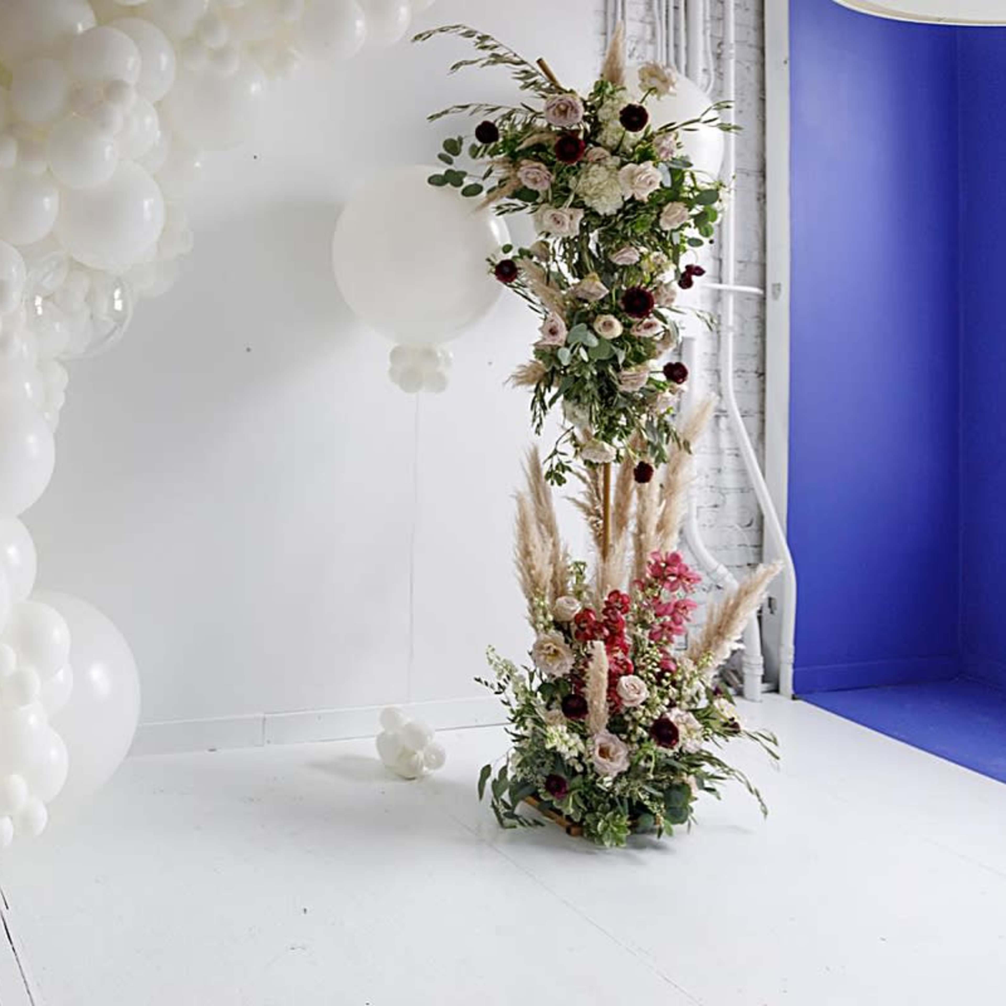 A white balloon installation beside a floral arrangement with various plants and flowers against a backdrop of blue and white walls.