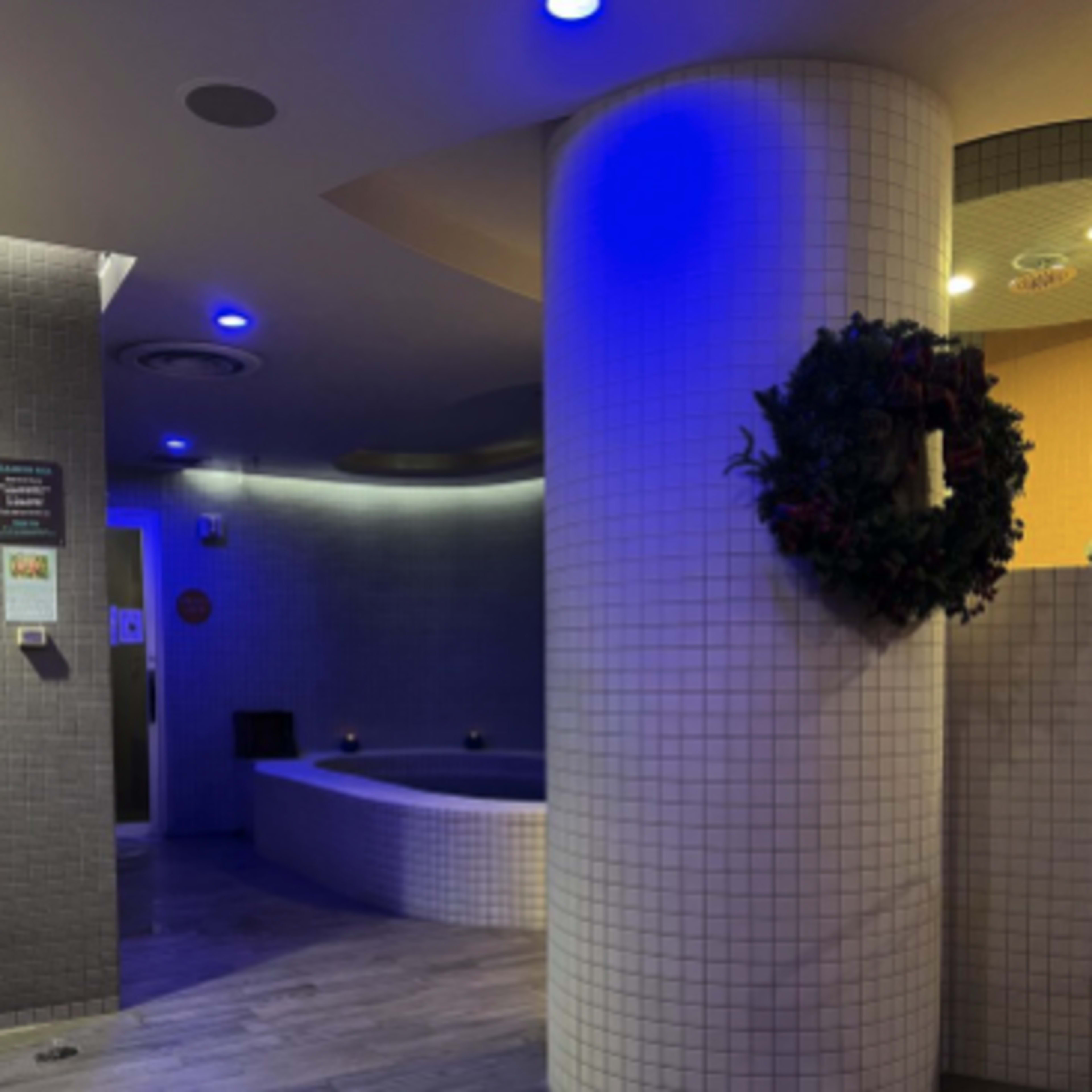 A spa area with blue lighting, a circular hot tub, and a column adorned with a holiday wreath.