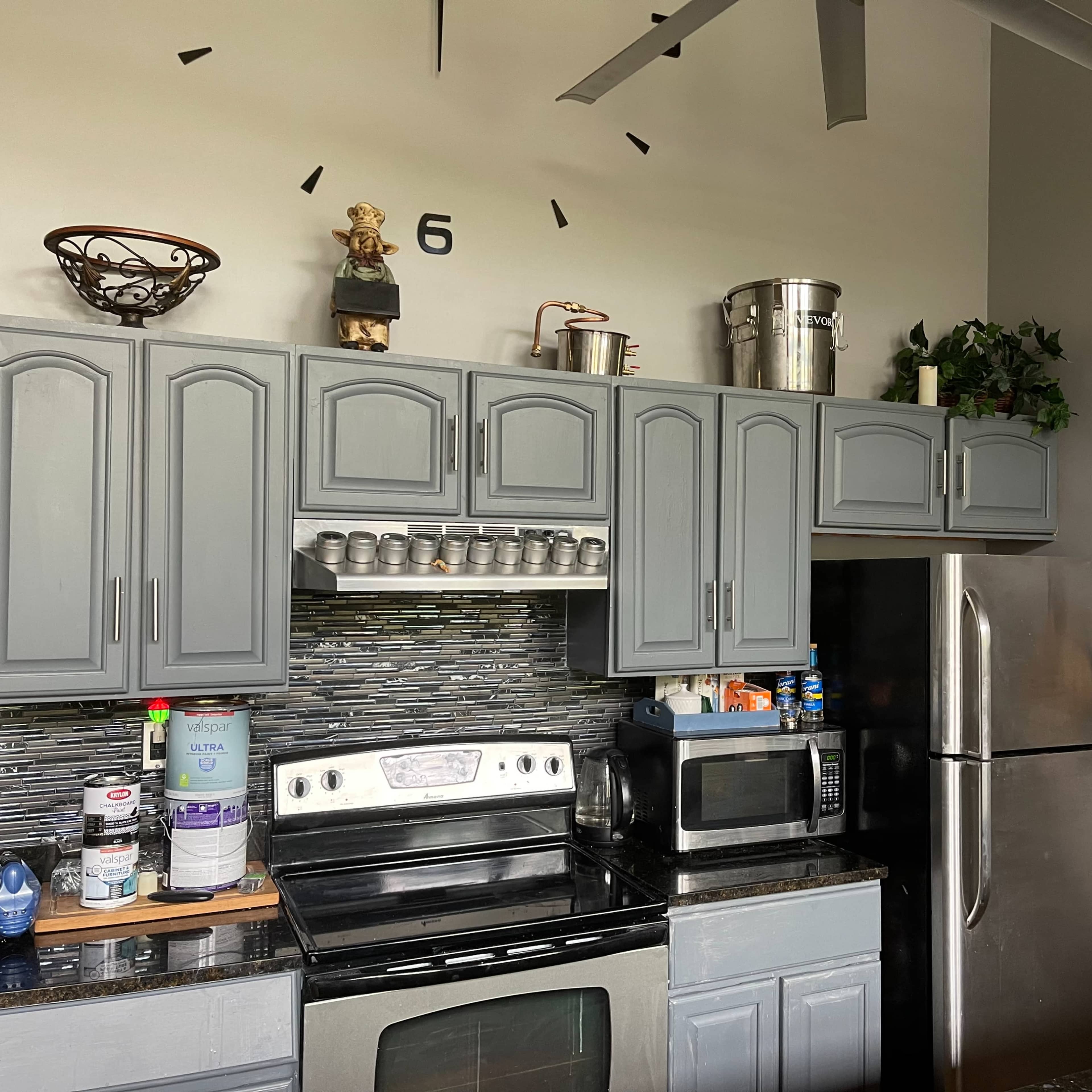 A modern kitchen features gray cabinets, a stainless steel refrigerator, an oven, and various kitchen items on the countertop.