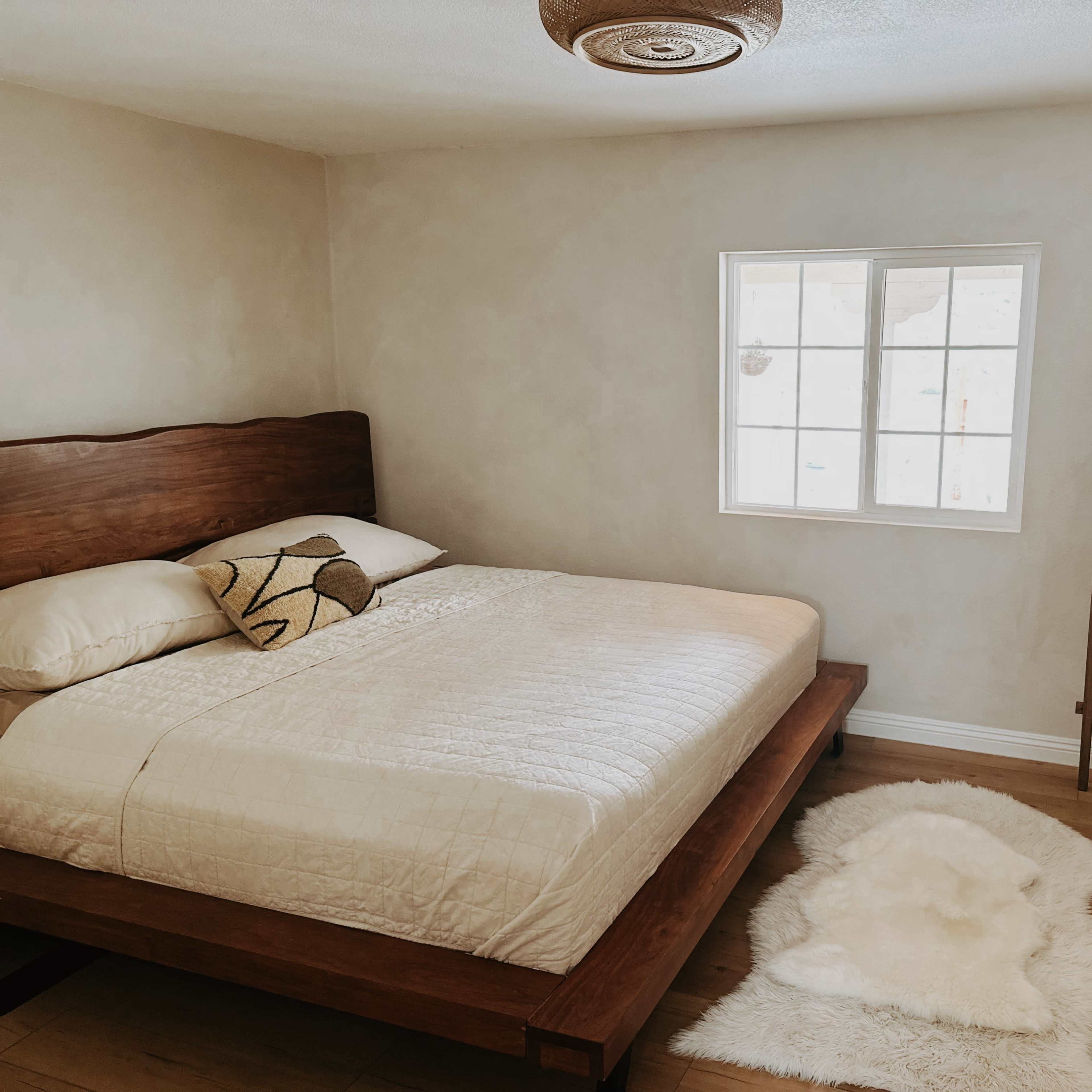 A simple bedroom featuring a wooden bed, a window, a decorative ladder, and a potted plant.