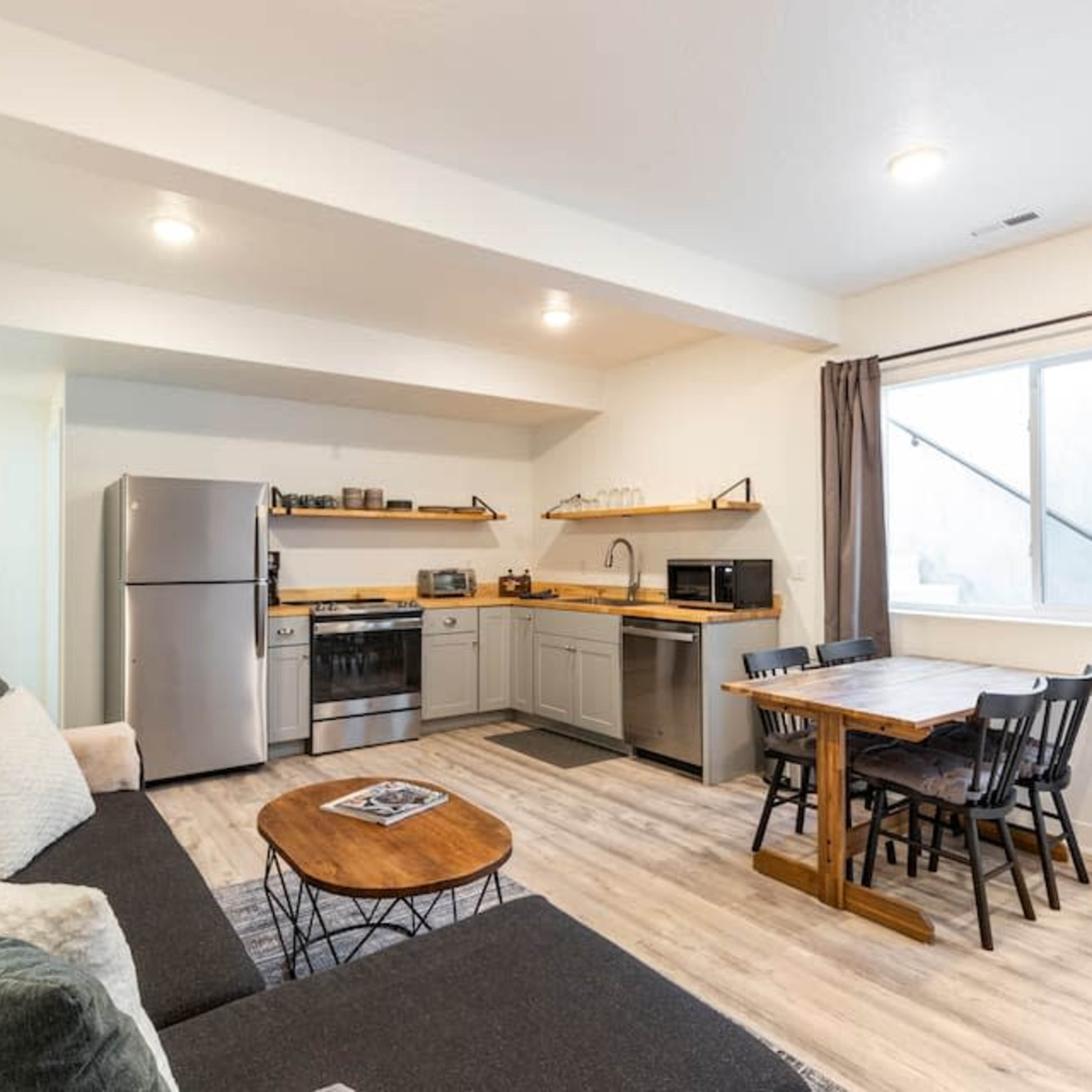 A modern living space featuring a kitchen area, a dining table with six chairs, a couch, and a refrigerator.
