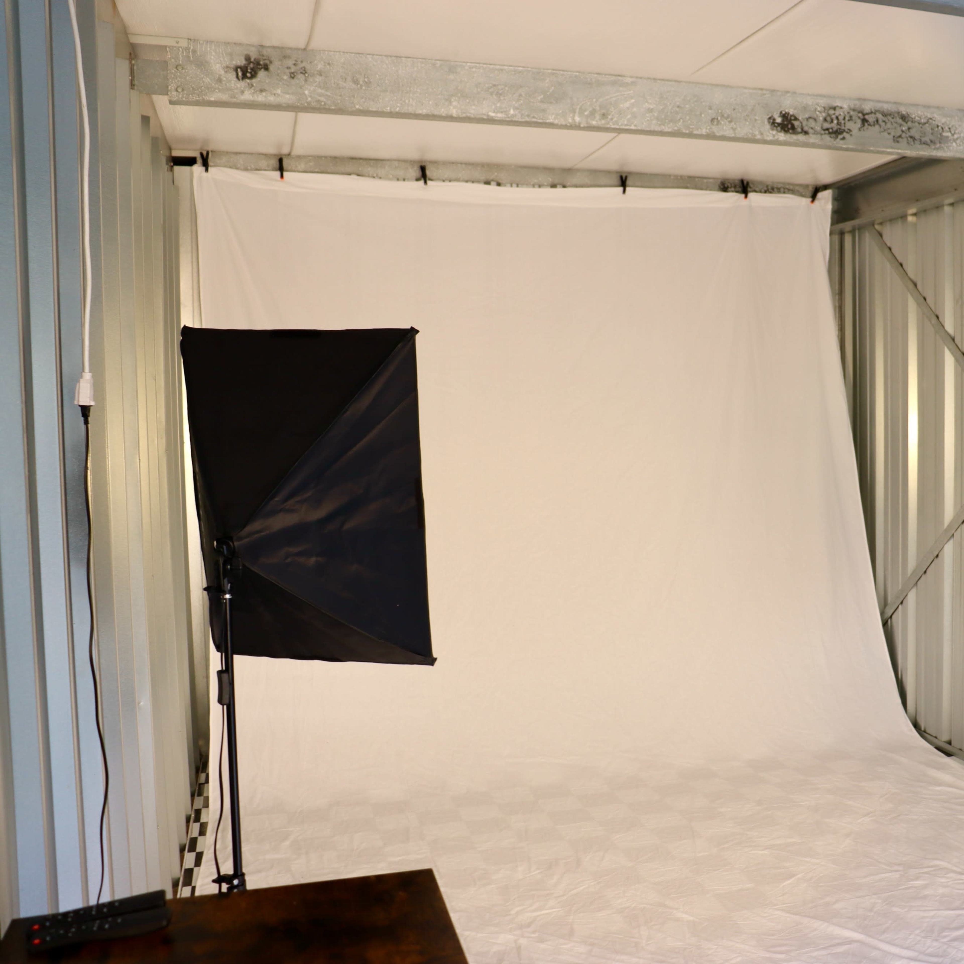 A photo studio with a white backdrop and two softbox lights set up on either side.