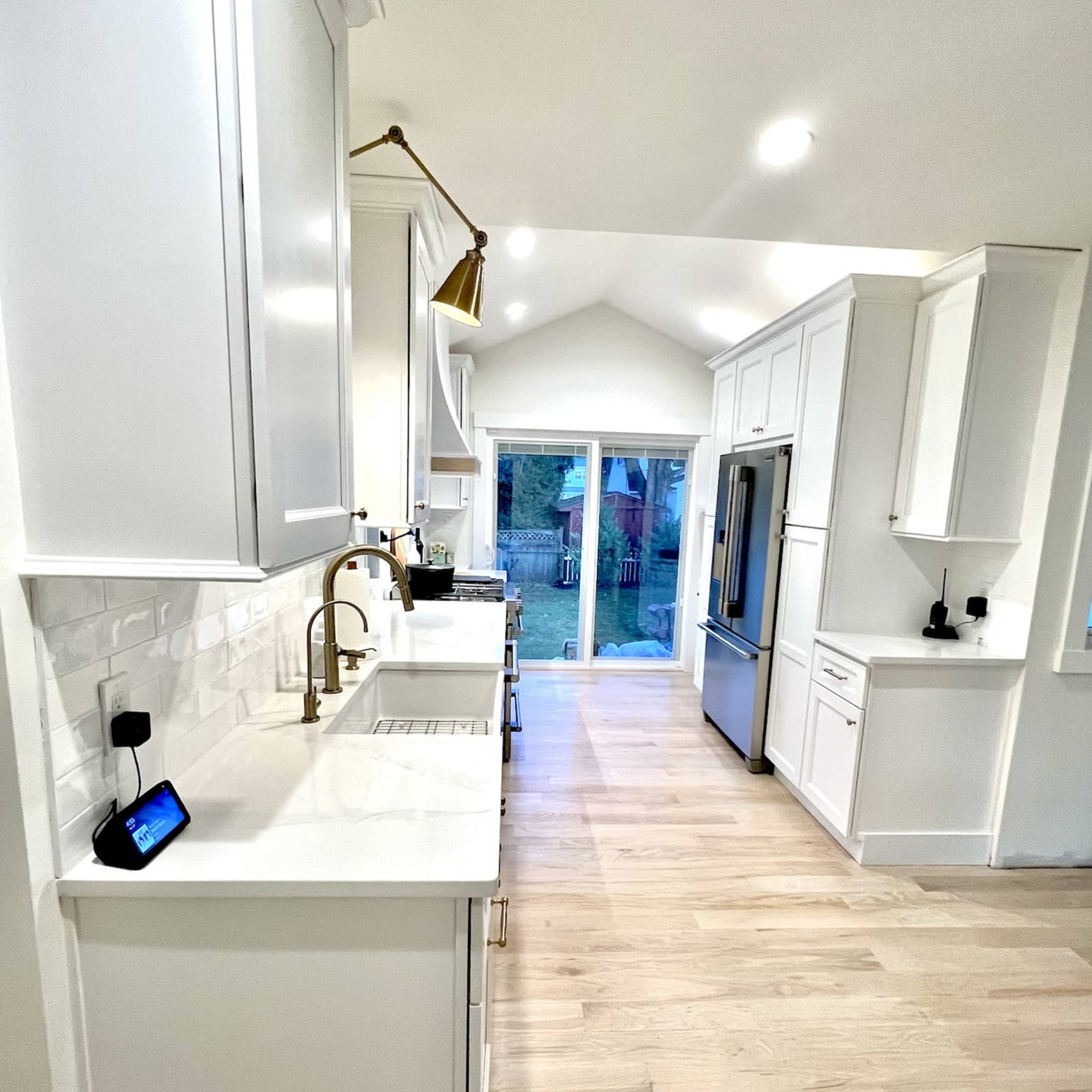 A modern kitchen features white cabinetry, a large sink, and stainless steel appliances, with a view of a patio through a sliding glass door.