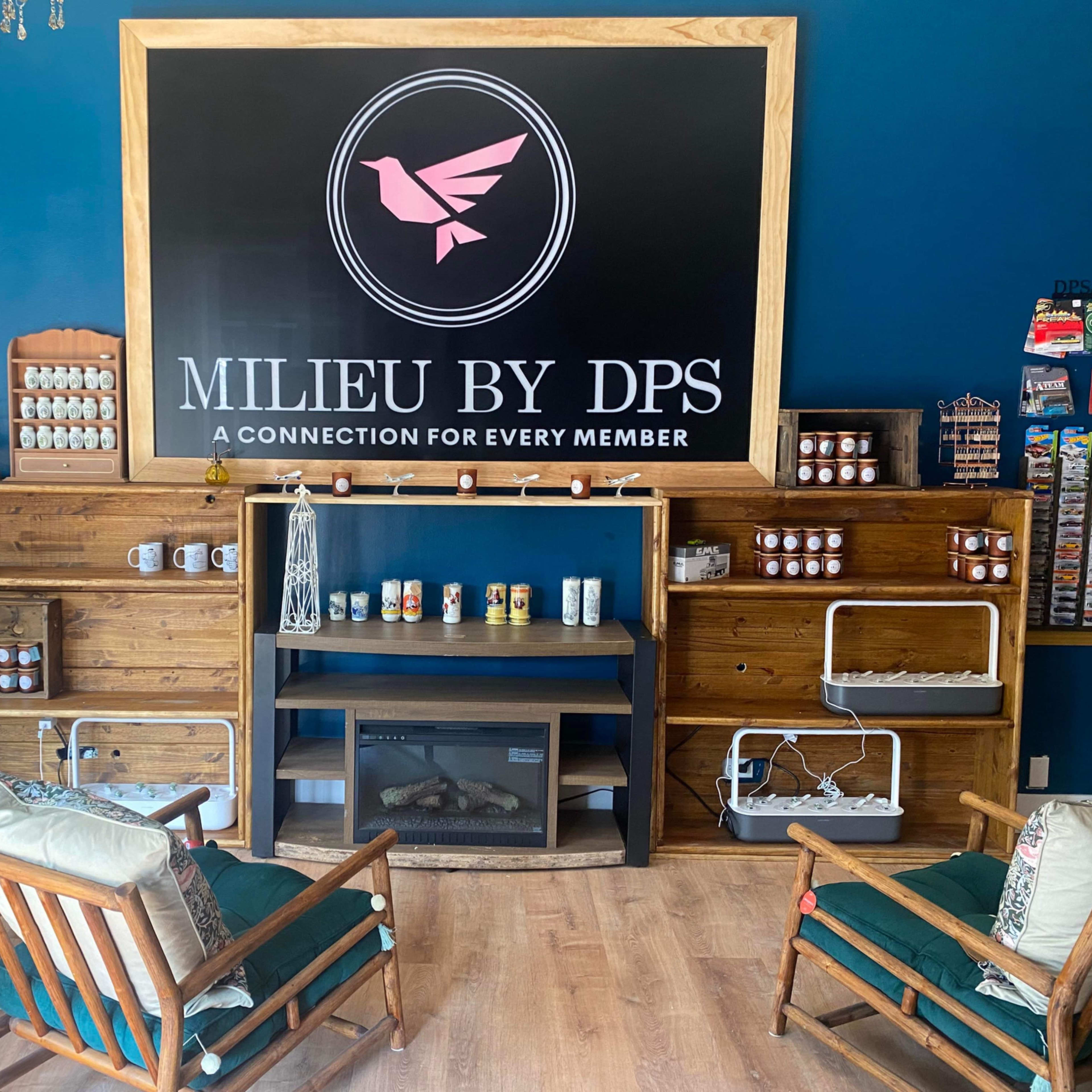 A cozy interior of a business space featuring wooden shelves, comfortable seating, and a large sign that reads "MILIEU BY DPS."