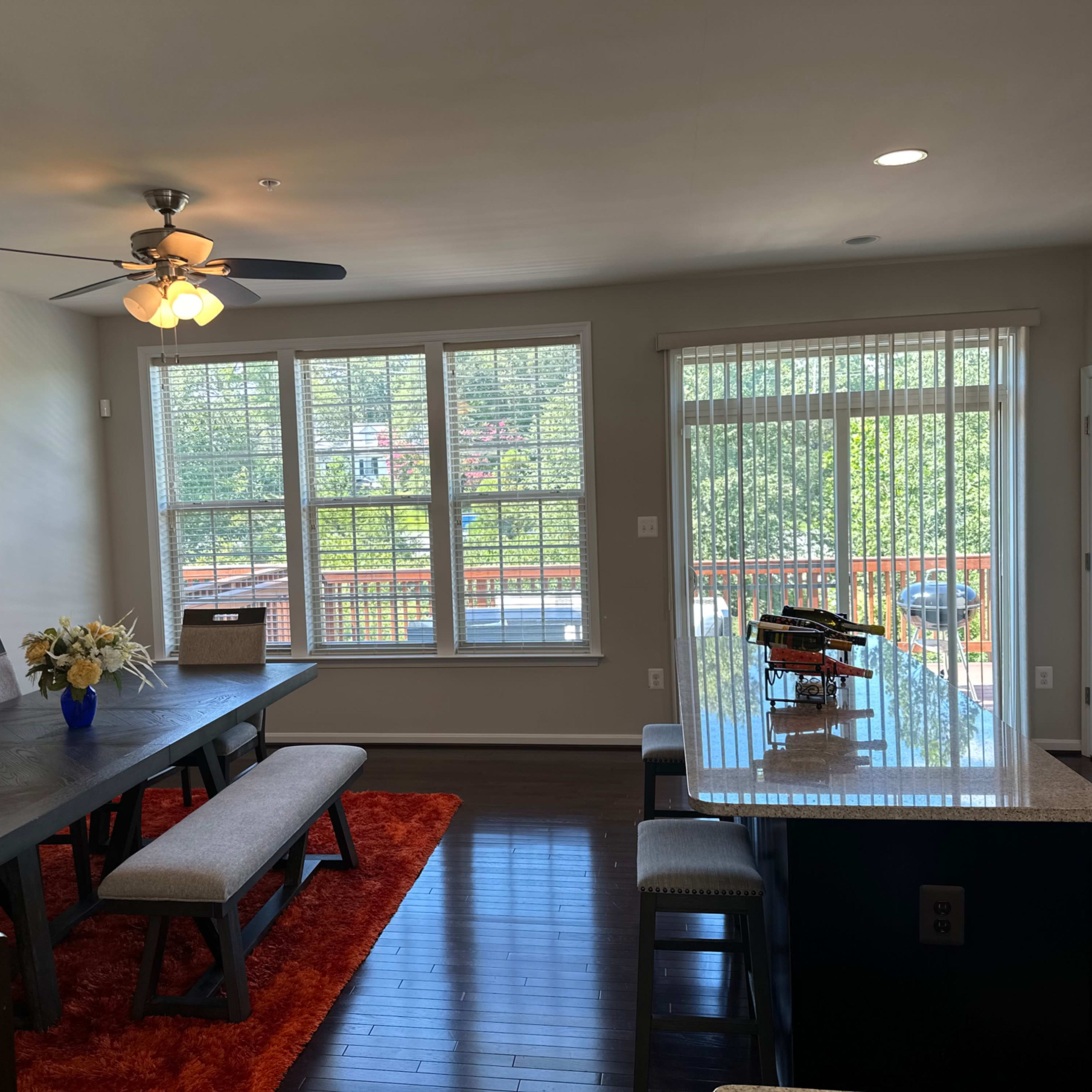 A modern dining room features a large table with benches, a kitchen island, and large windows allowing natural light to fill the space.