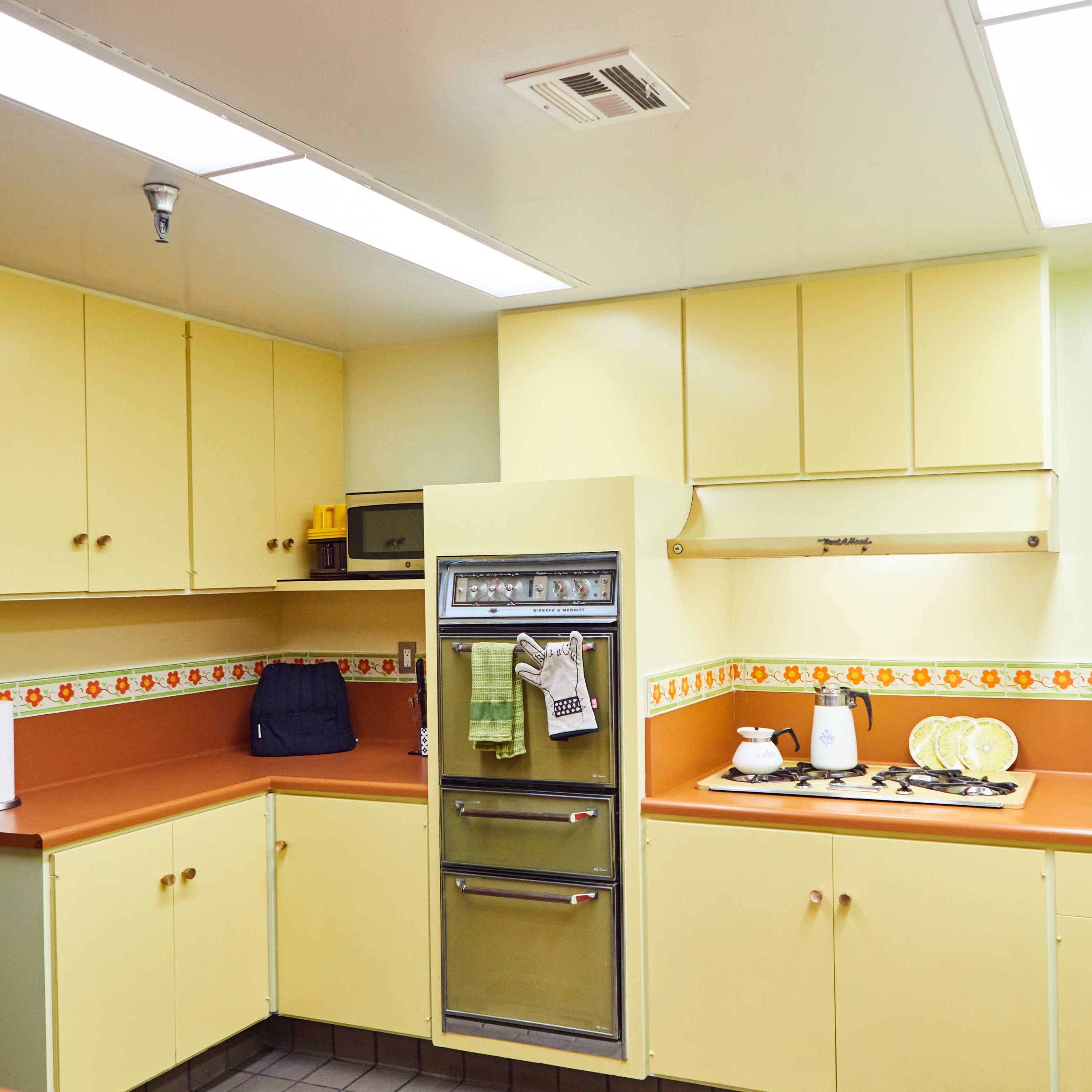 A kitchen with yellow cabinets, an orange countertop, and appliances including a refrigerator and stove.