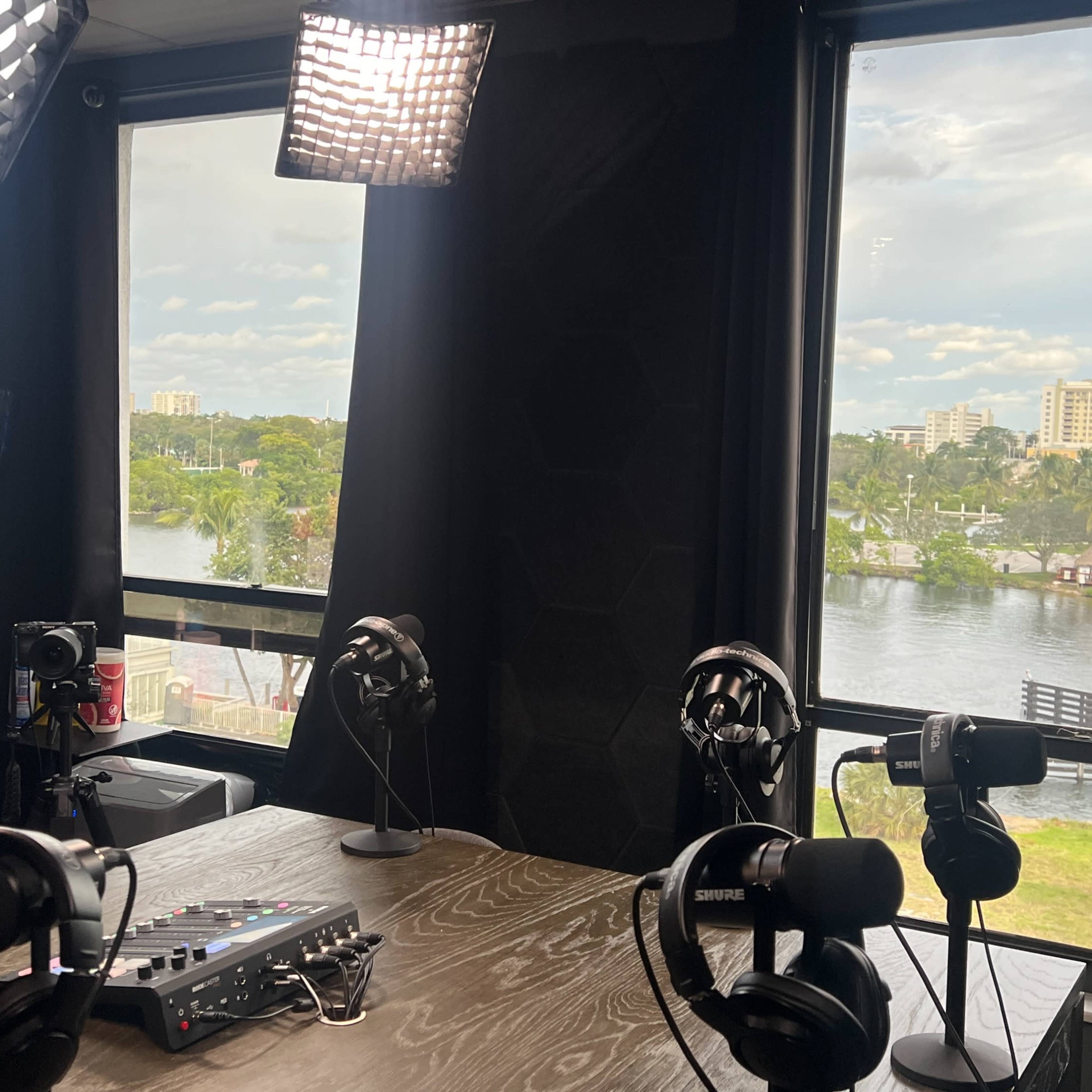 A radio studio with microphones and audio equipment facing large windows that overlook a scenic view of a river and city skyline.