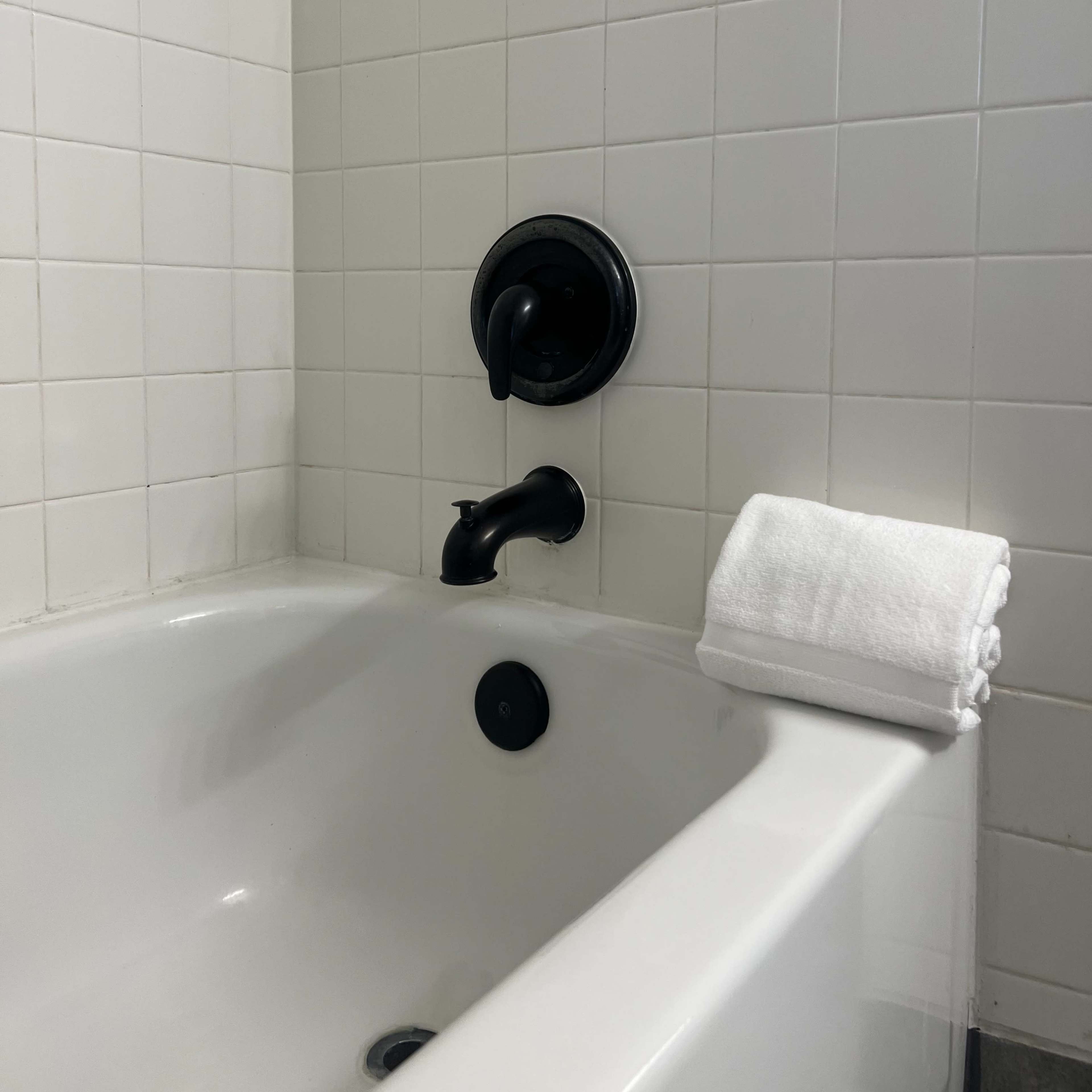 A corner of a bathtub with a black faucet and a neatly folded white towel on the edge.