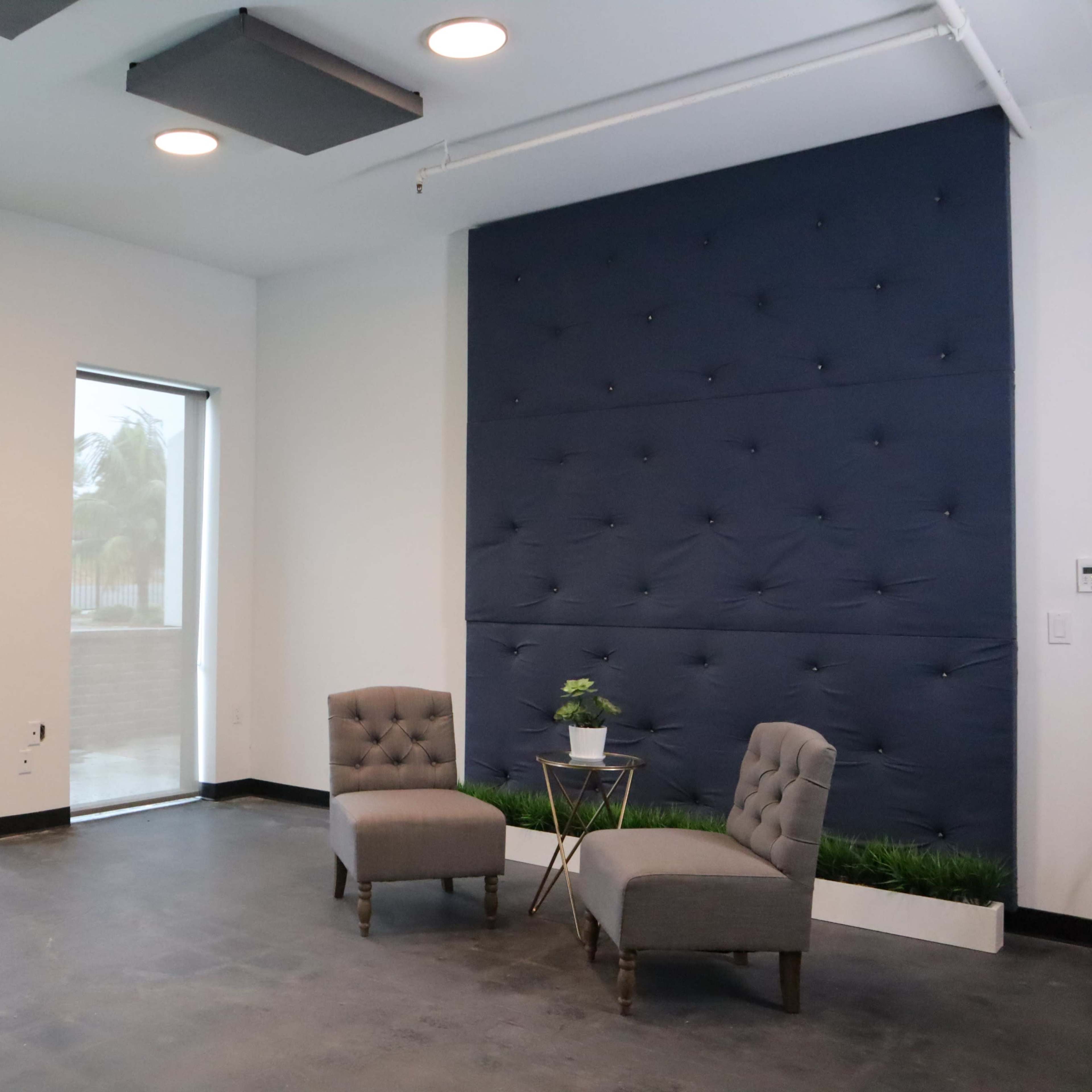A modern interior space with two upholstered chairs, a small table with a plant, and large windows overlooking a landscaped area.