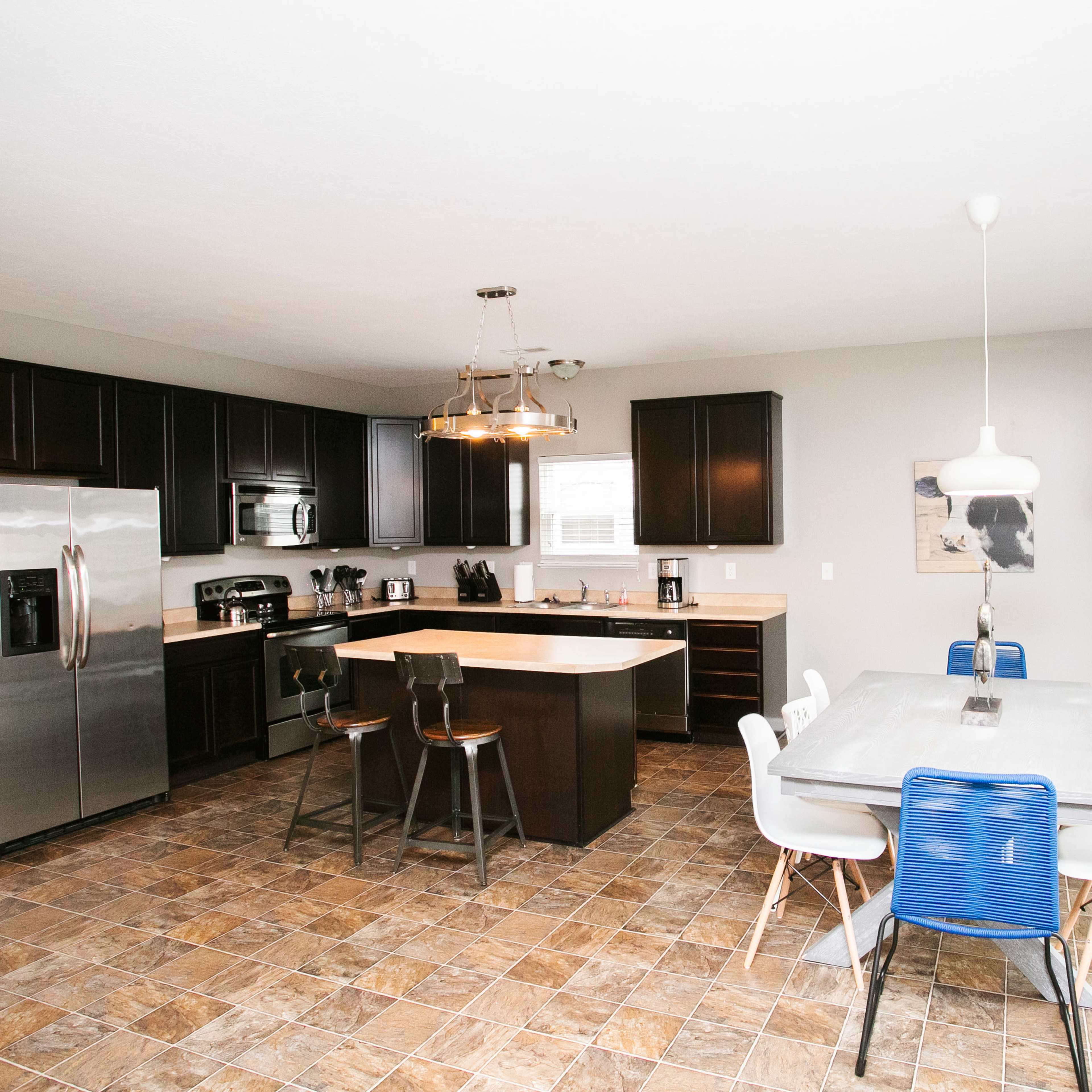 A modern kitchen with dark cabinetry, stainless steel appliances, and a dining area featuring a rectangular table and chairs.