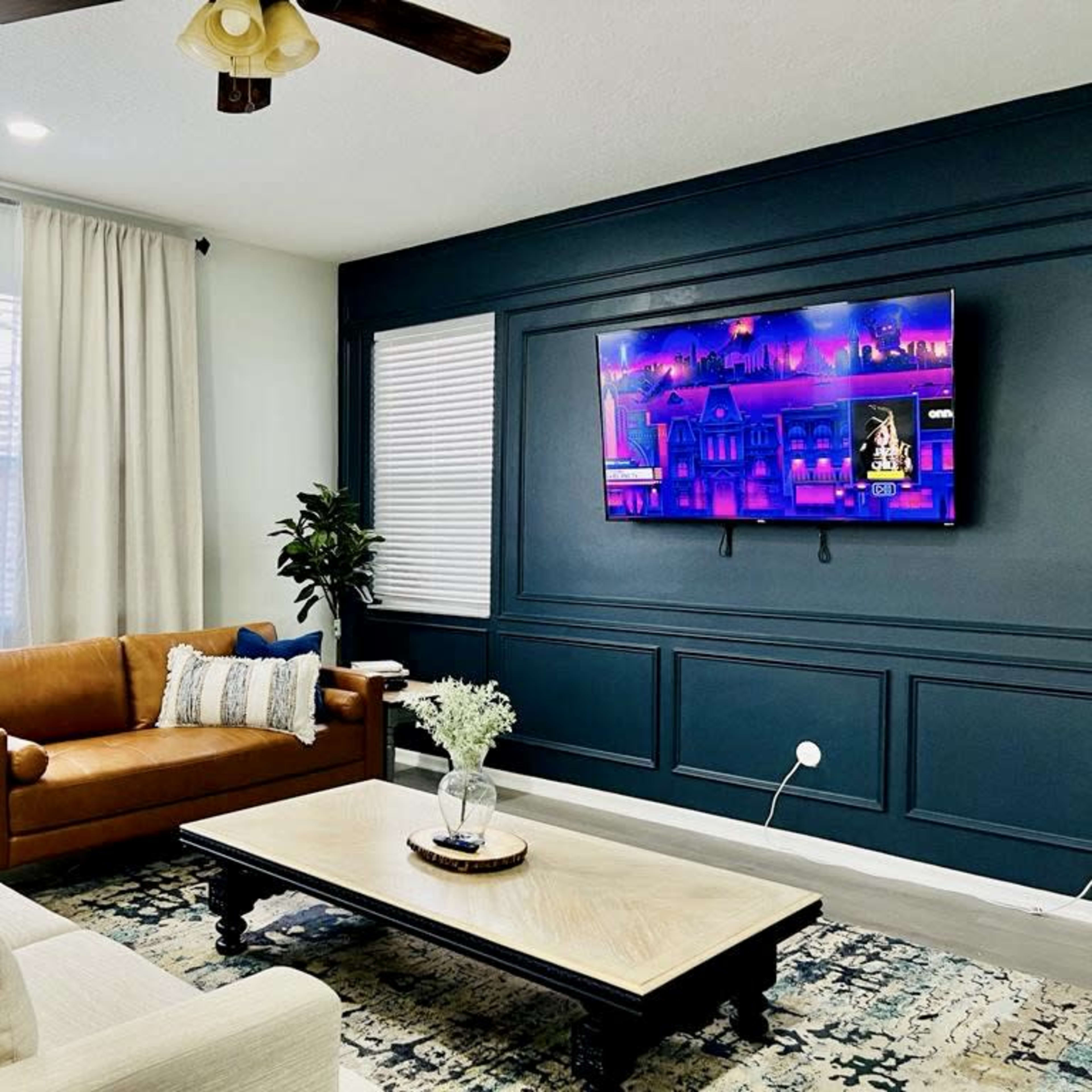 The living room features a light-colored sofa, a brown leather couch, a coffee table, and a television mounted on a dark blue accent wall.