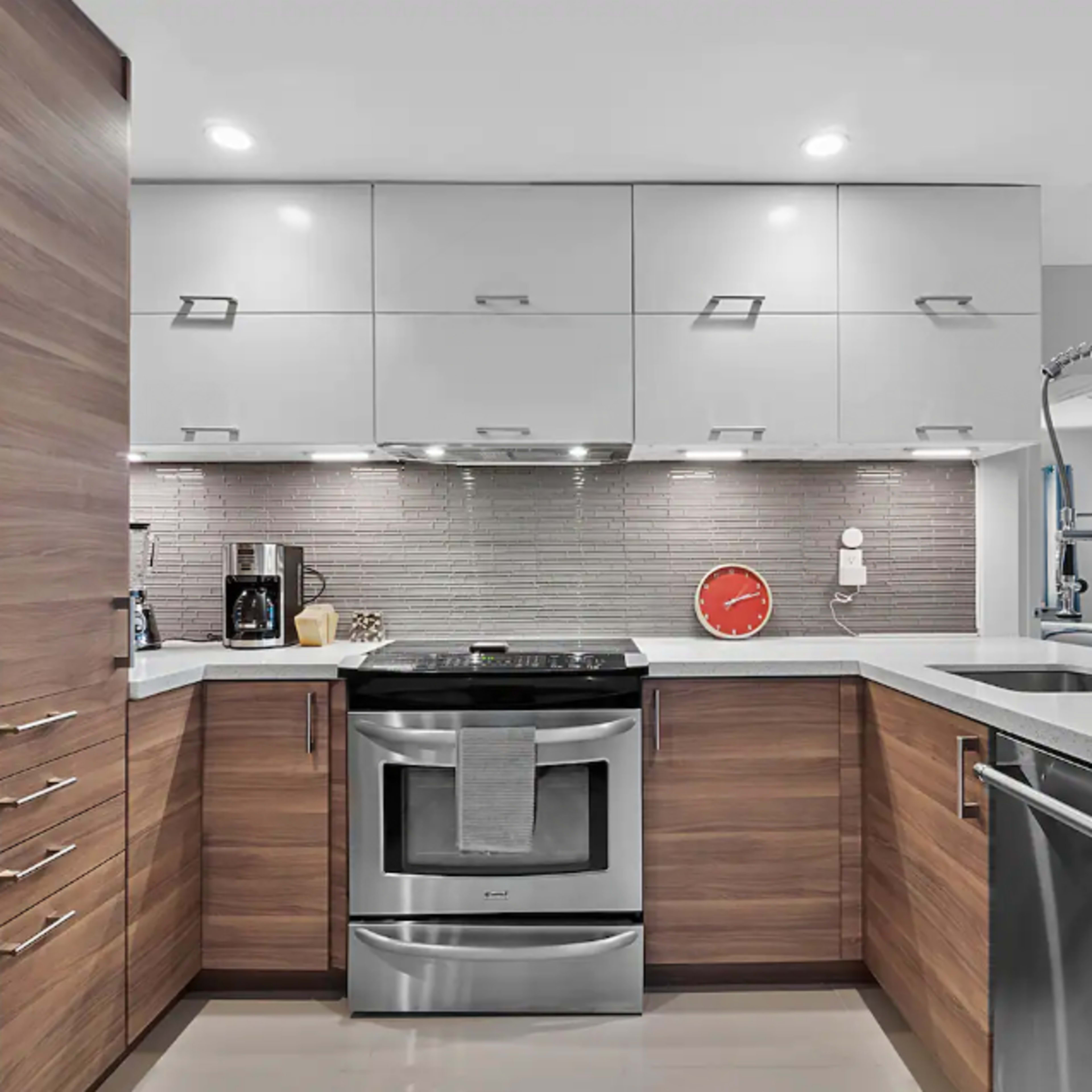 A modern kitchen with stainless steel appliances, wood cabinetry, and a light-colored countertop.