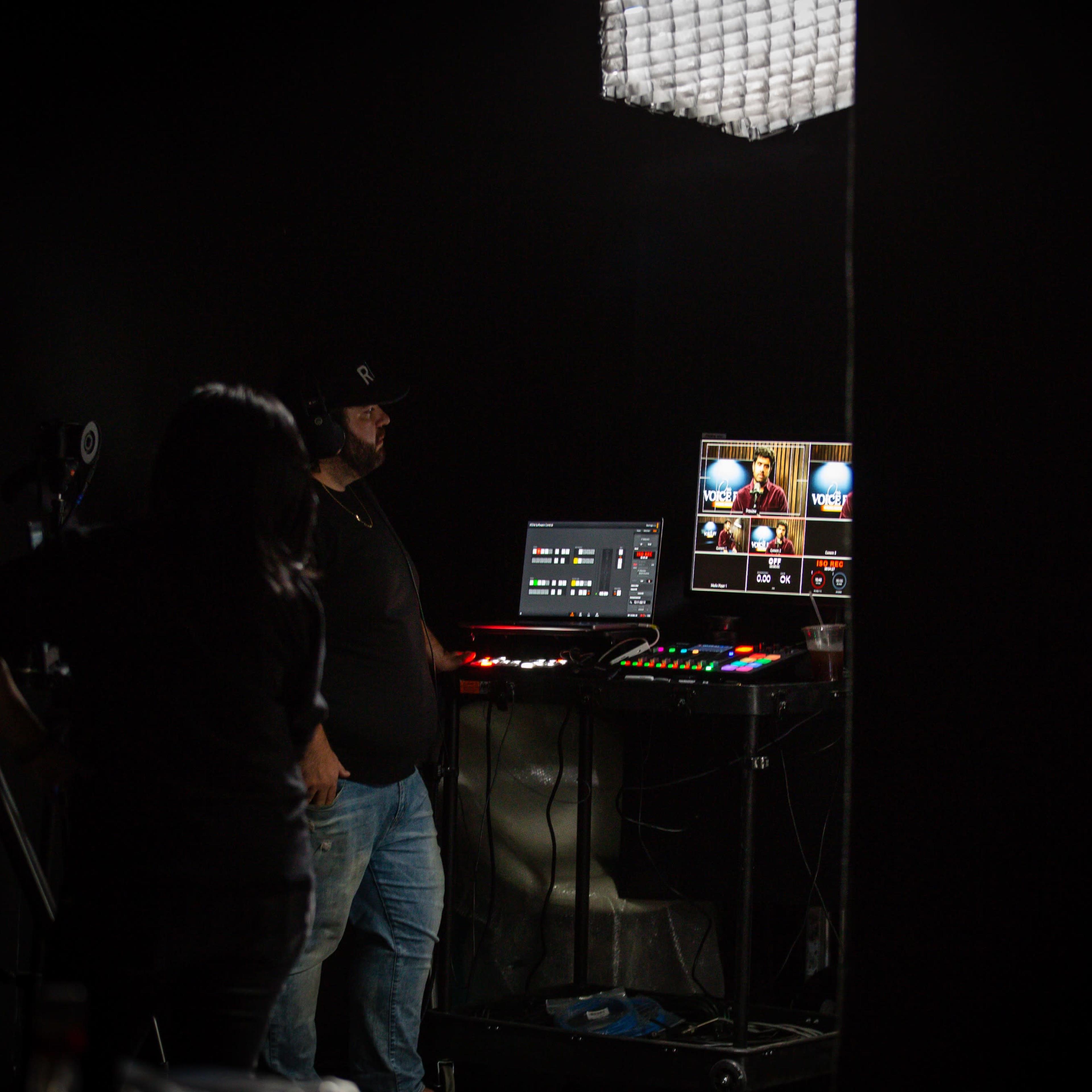 A person operates a video production setup in a dimly lit room.