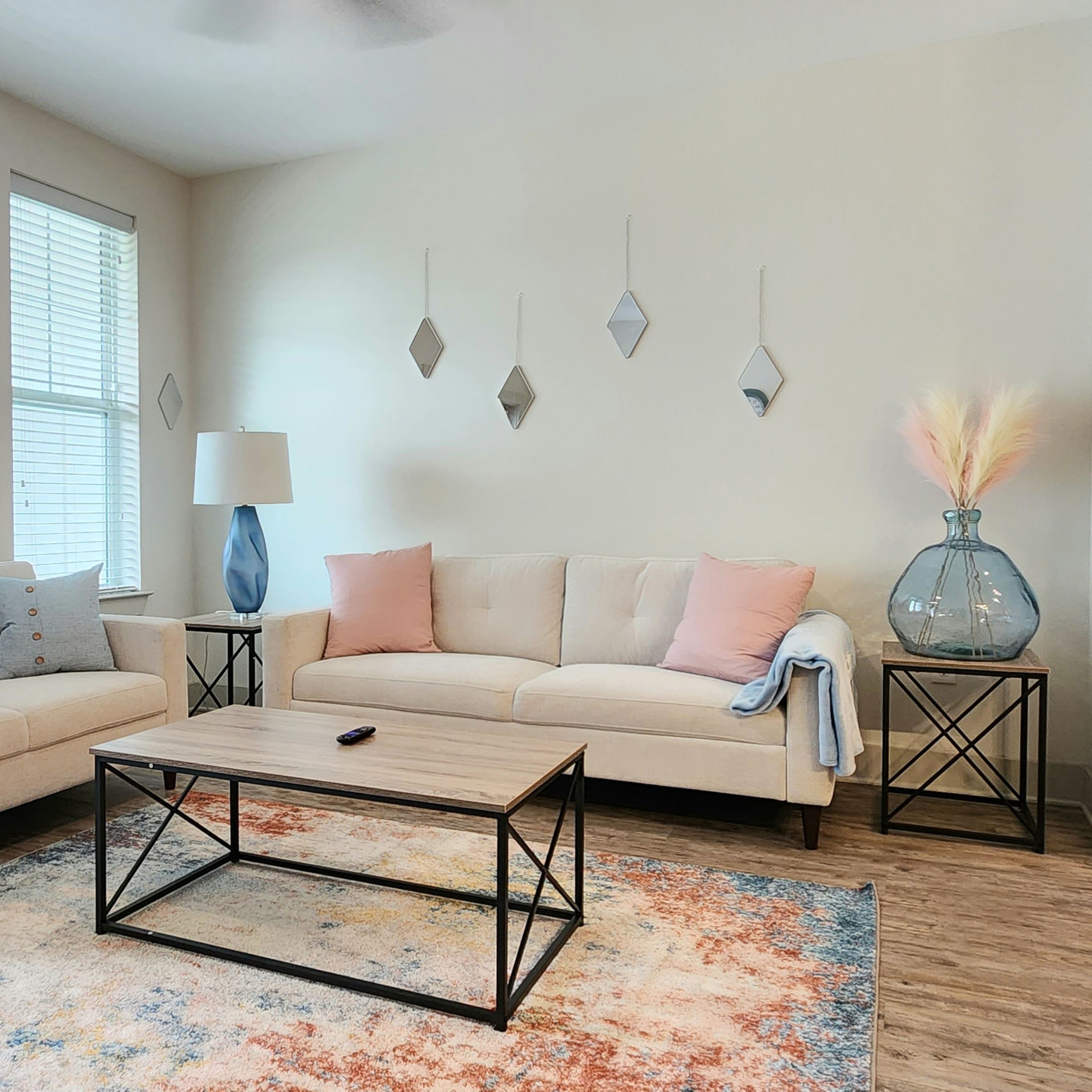 A modern living room featuring a beige sofa and loveseat, a glass coffee table, and decorative elements like a floor lamp and a large vase.