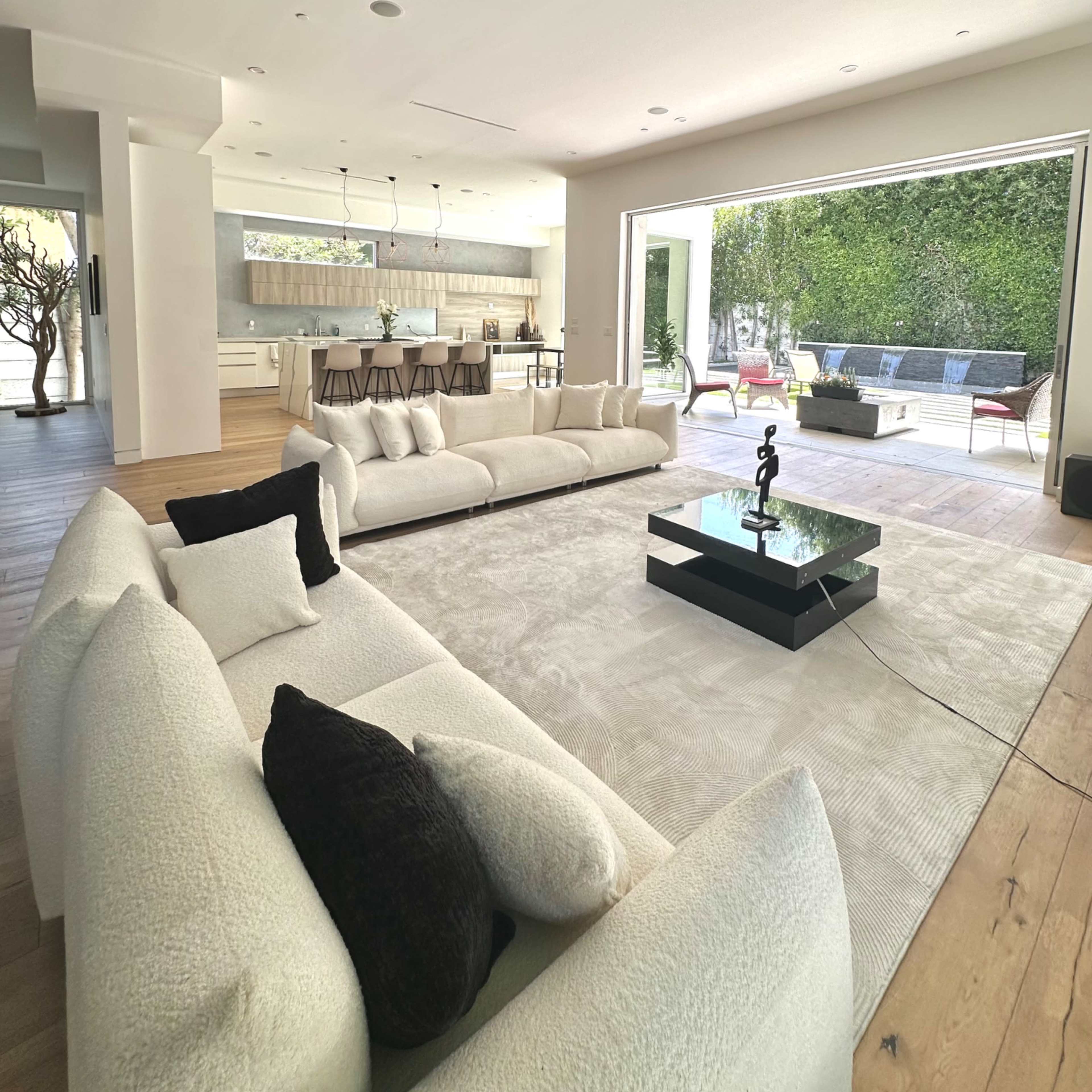 A modern living room with a large white sectional sofa, a black coffee table, and an open layout leading to a patio with outdoor seating.