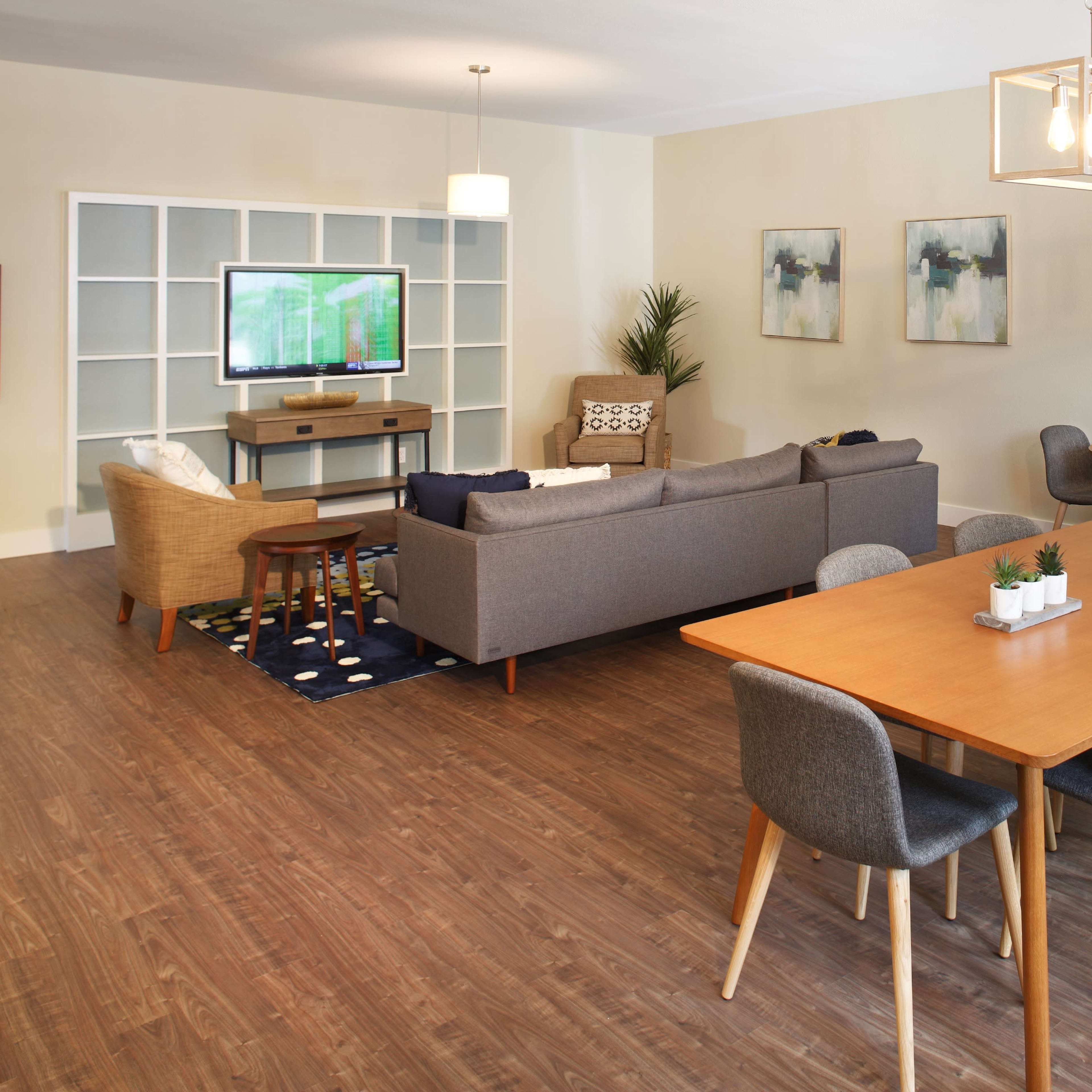 A modern living room features a sofa, coffee table, and television against one wall, with a dining table and chairs on the other side.