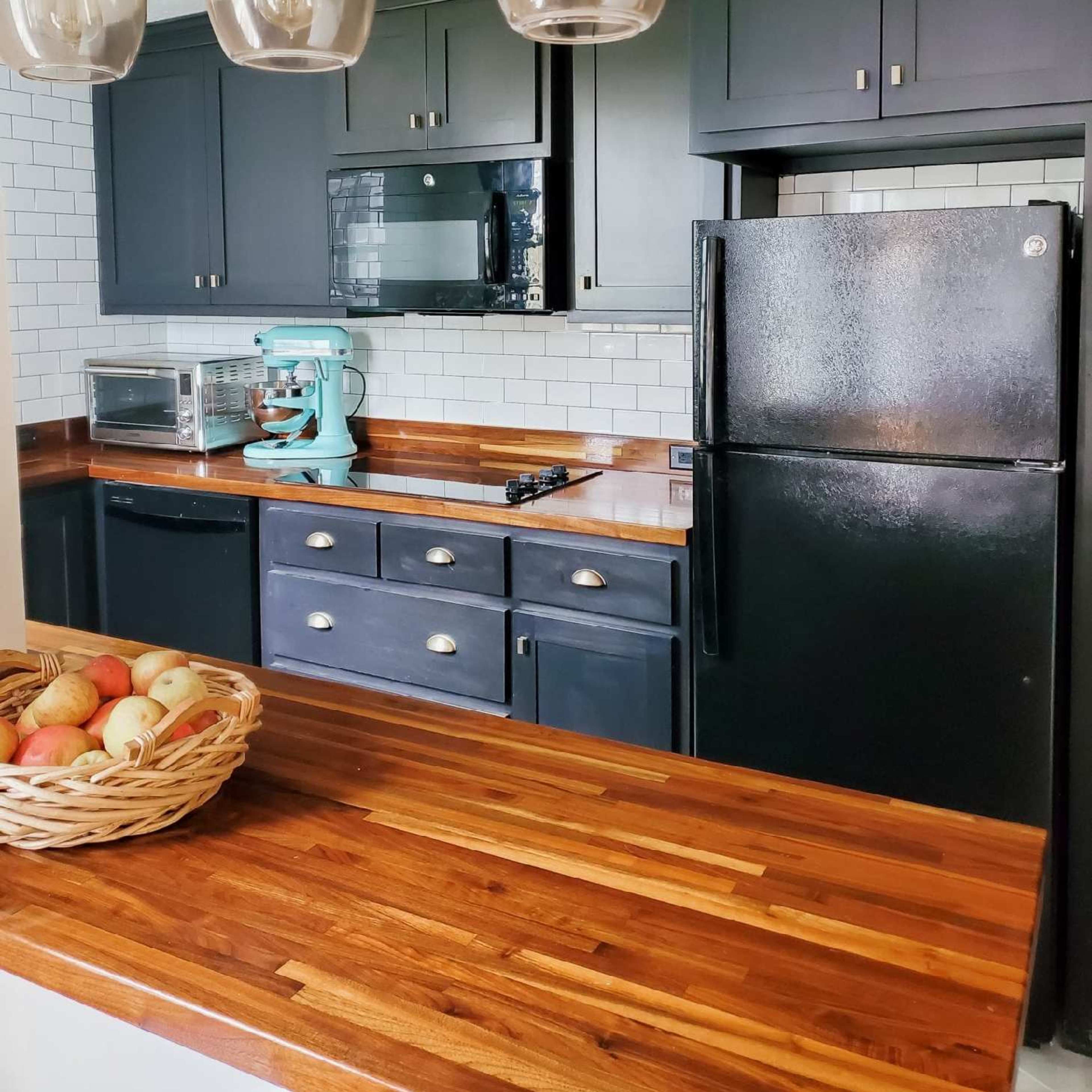 The kitchen features dark cabinets, a wooden countertop, and a black refrigerator, with a turquoise stand mixer and a bowl of apples on the counter.