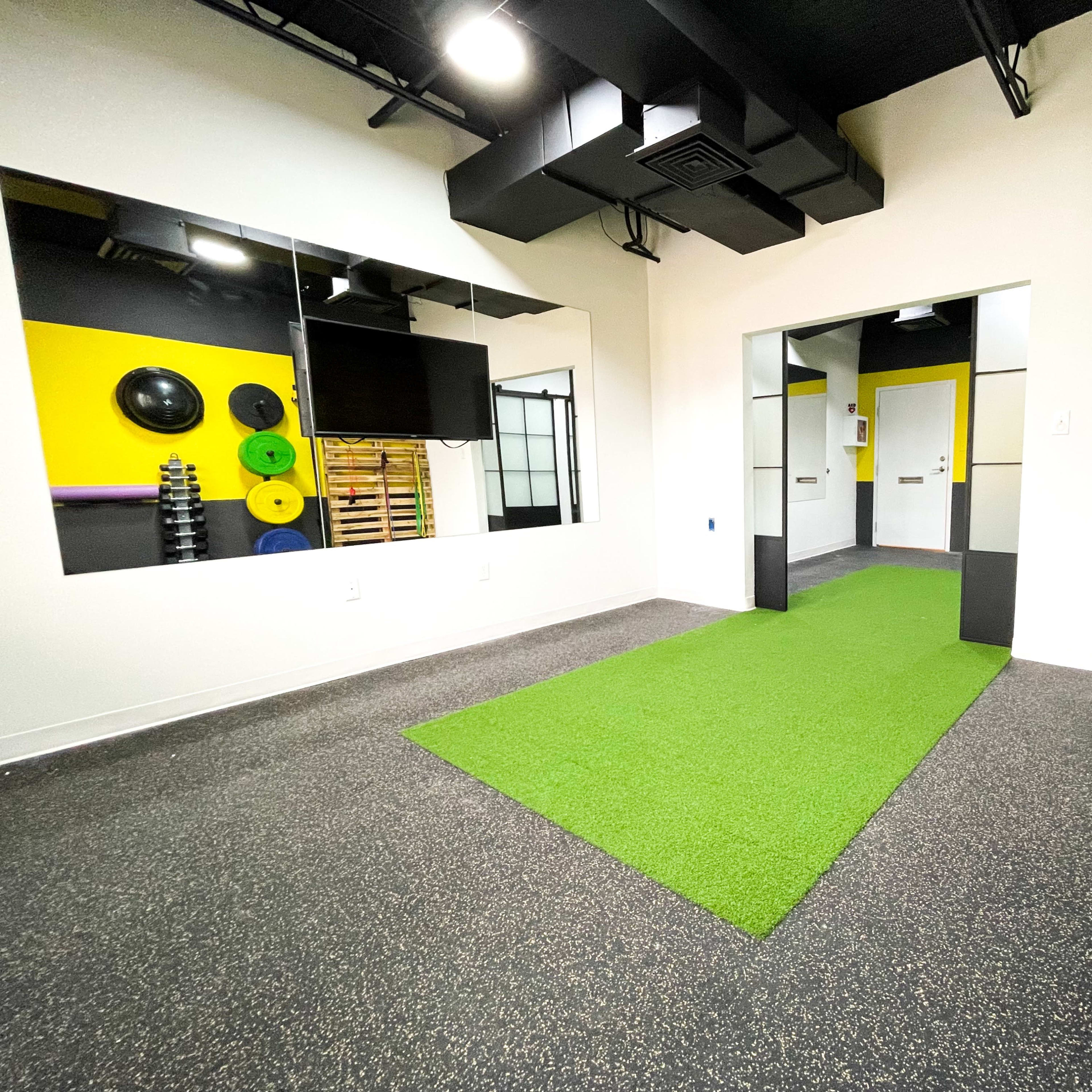 A modern gym interior featuring a green turf pathway, mirrored walls, and exercise weights mounted on a rack.