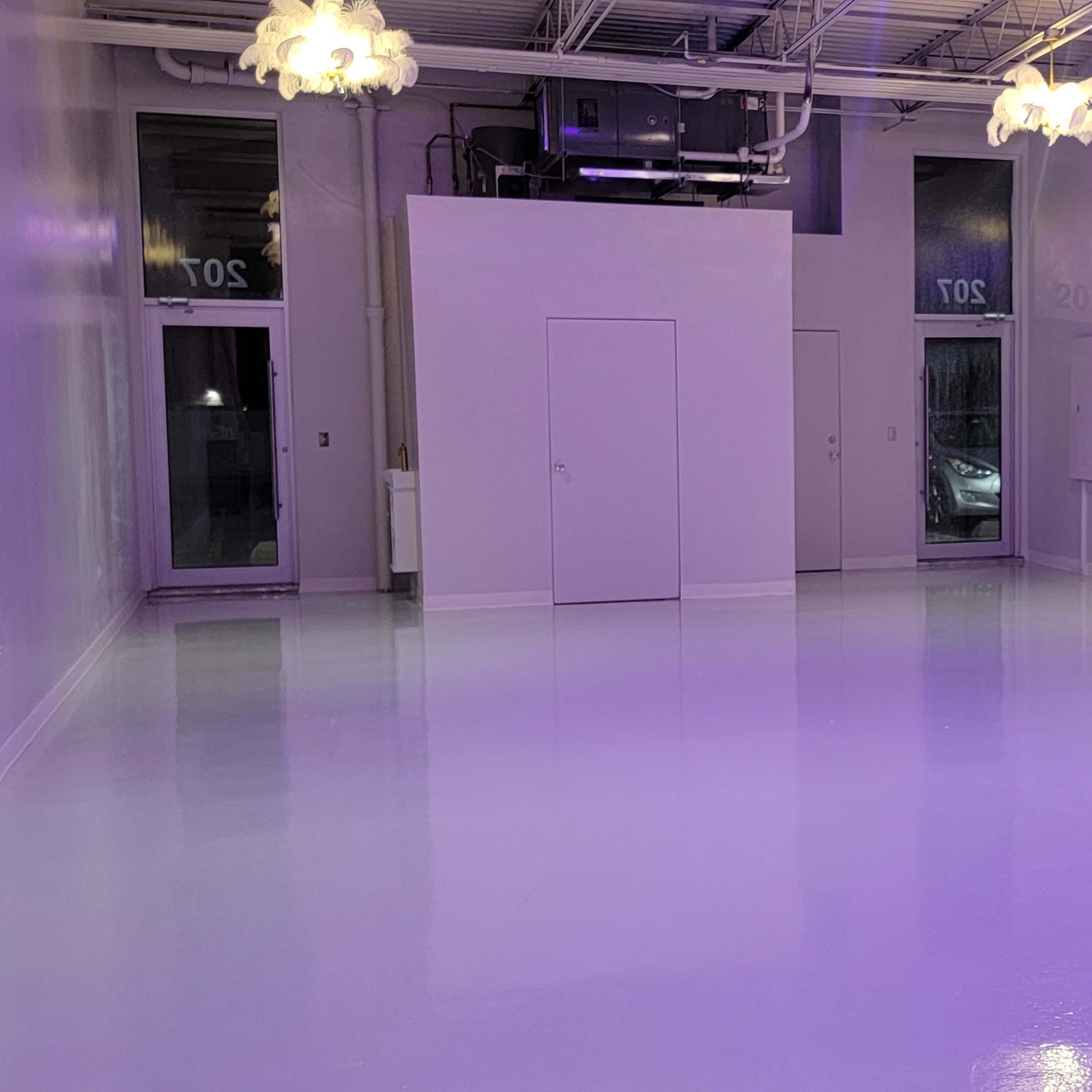A spacious, empty room with glossy white flooring and soft purple lighting, featuring two doors on one side.
