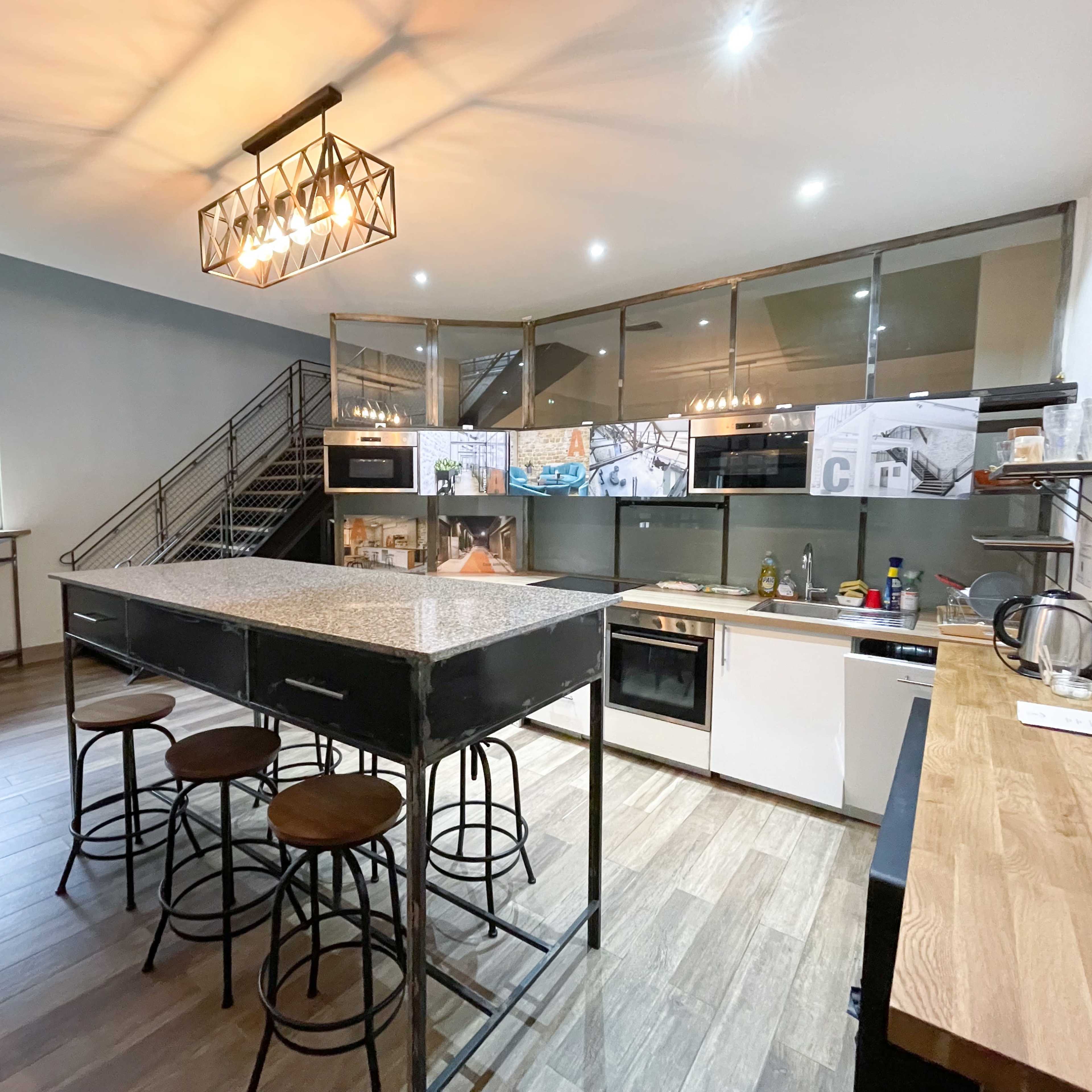 A modern kitchen with a large central island, dark cabinetry, and stainless steel appliances.