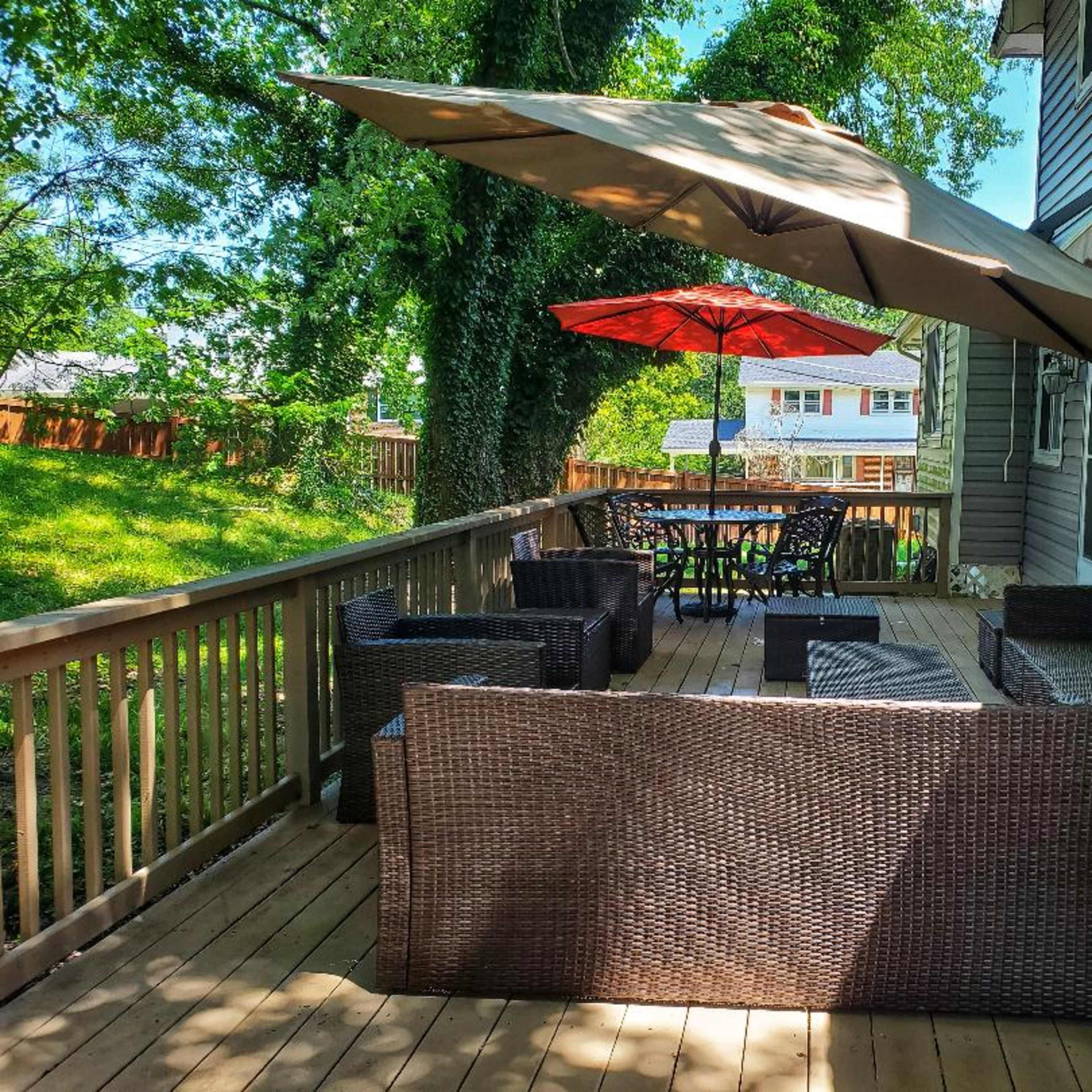 A wooden deck featuring a seating area with wicker furniture, a large umbrella, and a dining table set up in the background.