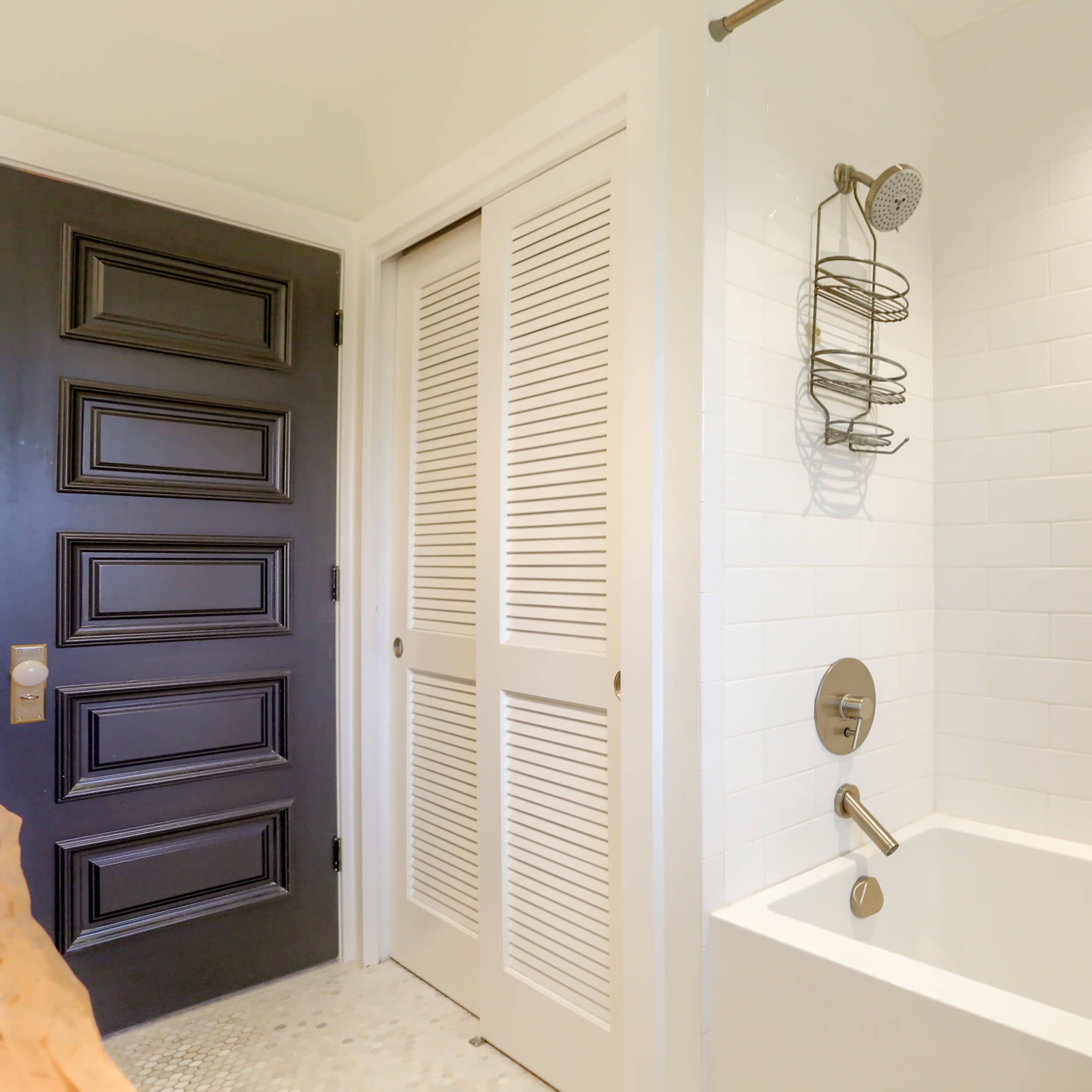 A bathroom featuring a white tiled shower area, a bathtub, and a black door leading to an adjacent space.