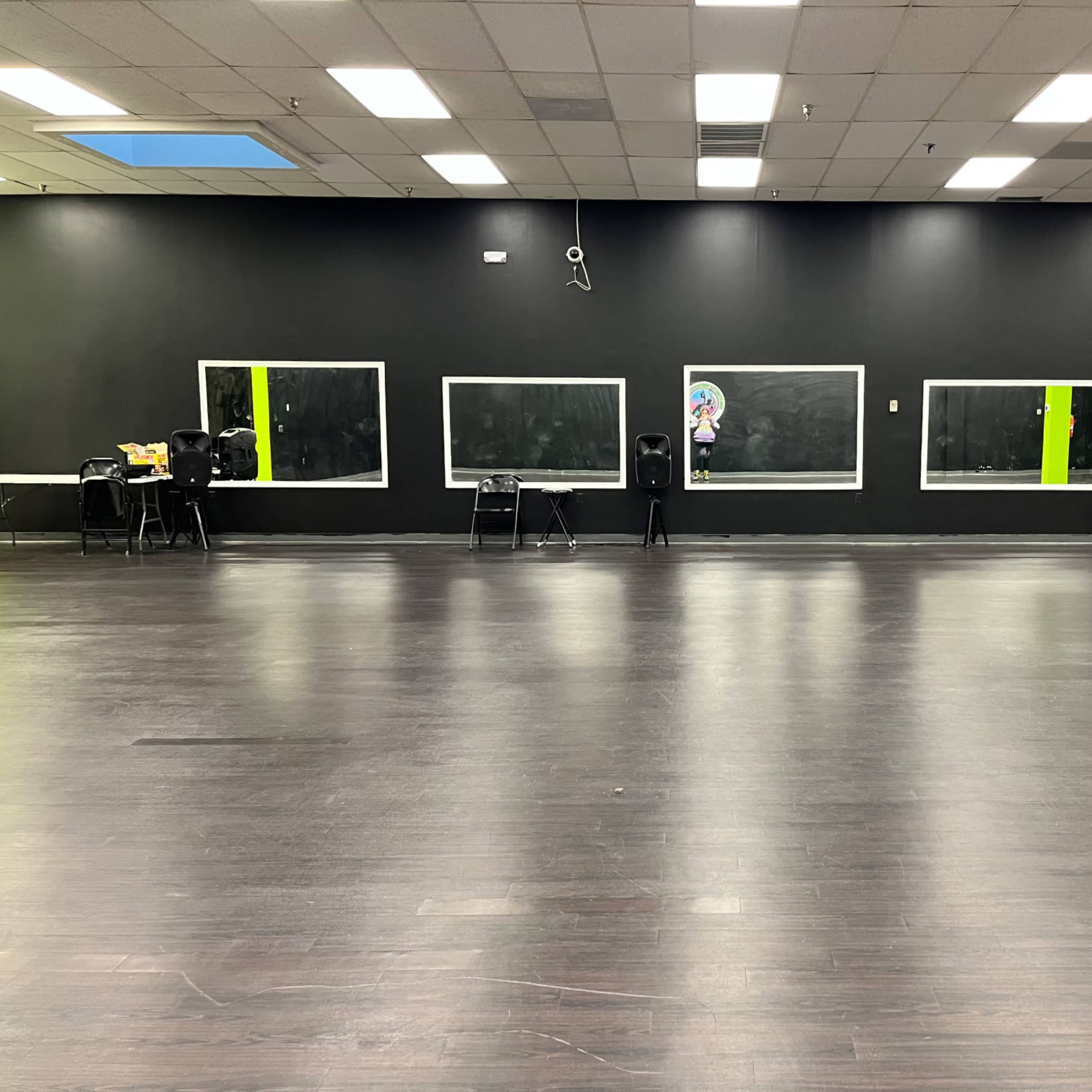 A large, empty dance studio with dark walls, wooden floors, and several mirrors.