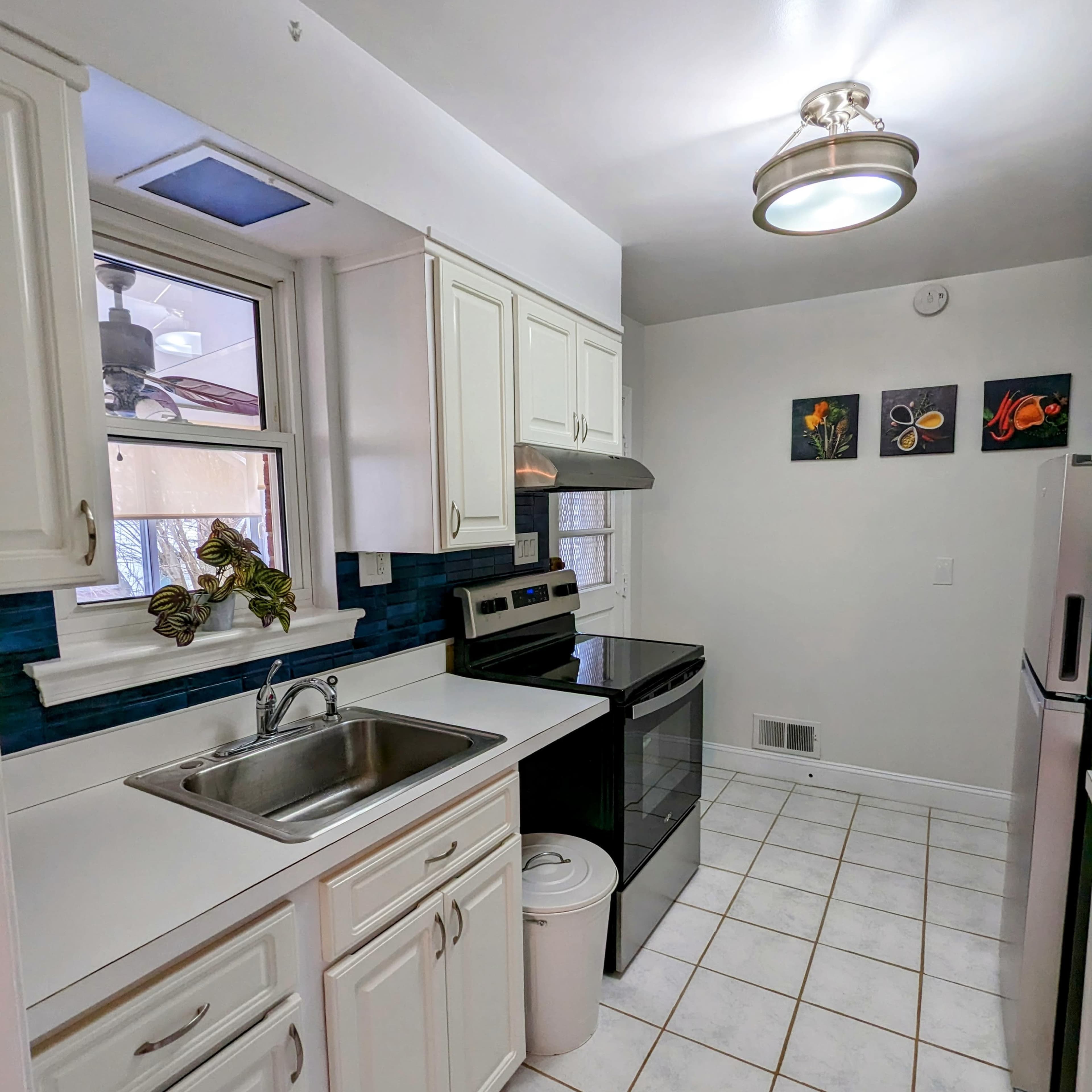 A compact kitchen features white cabinetry, stainless steel appliances, and a window that provides natural light.