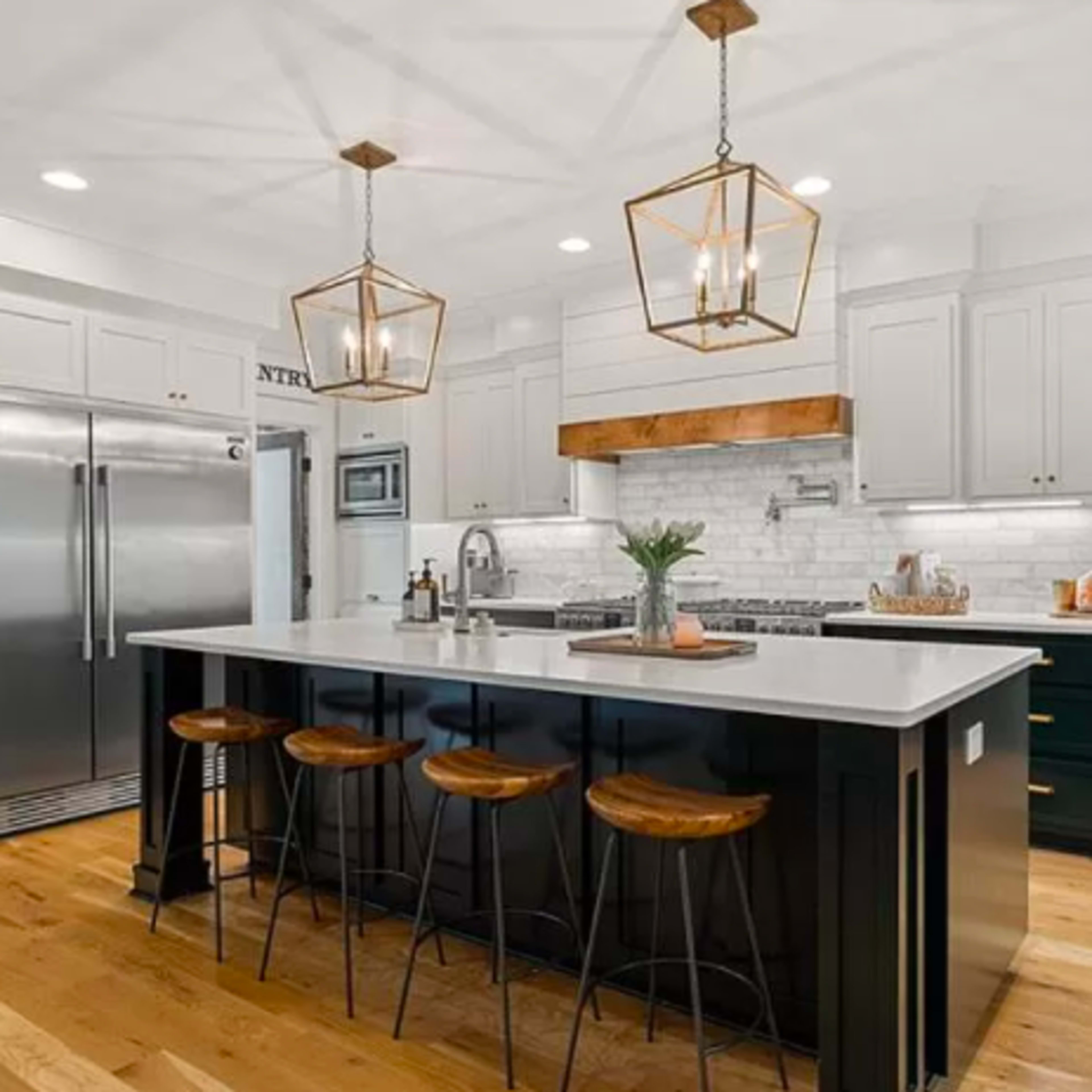 A modern kitchen features a central island with bar stools, stainless steel appliances, white cabinetry, and wooden accents on the countertops and ceiling lights.