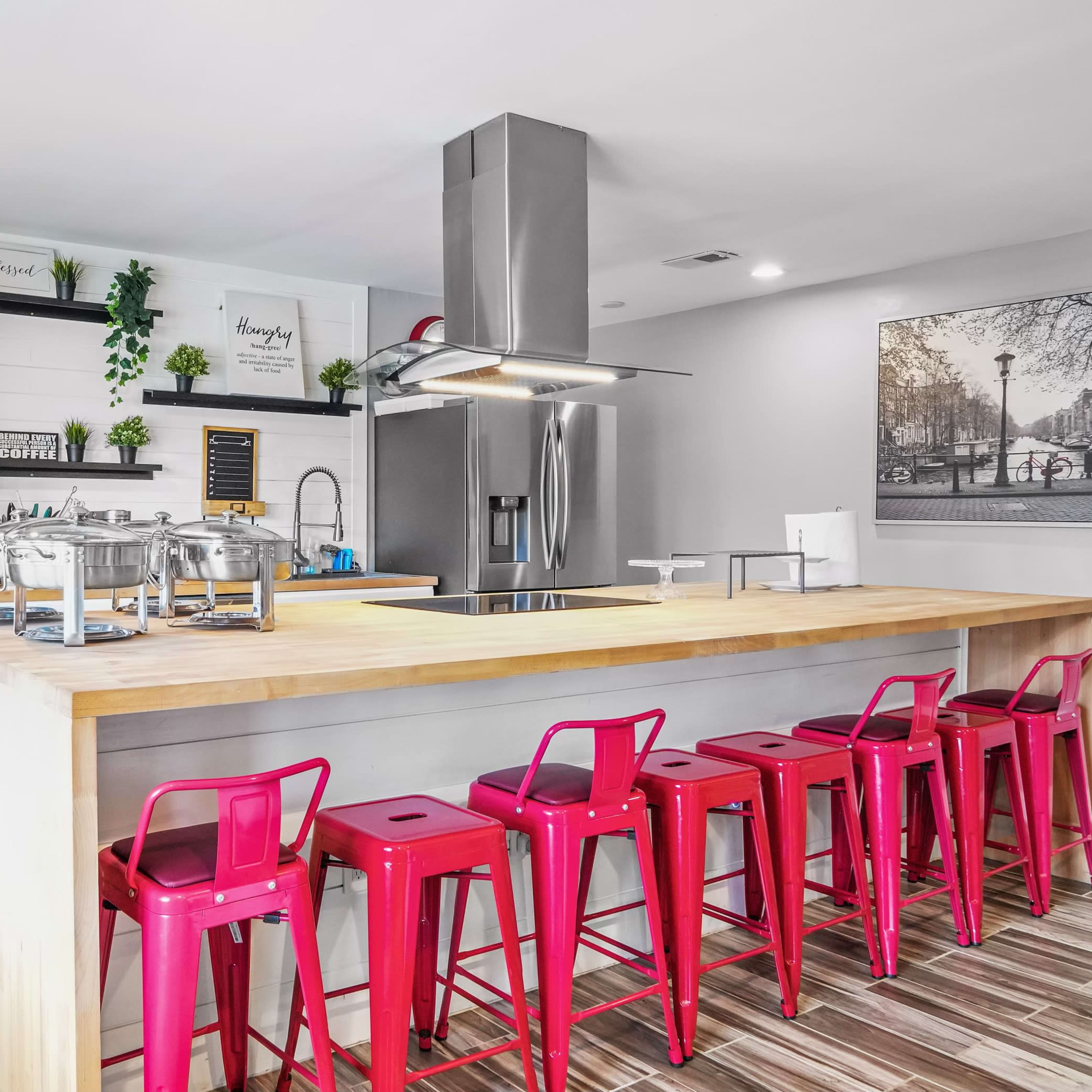 A modern kitchen features stainless steel appliances, a large wooden countertop, and red metal bar stools arranged around the island.