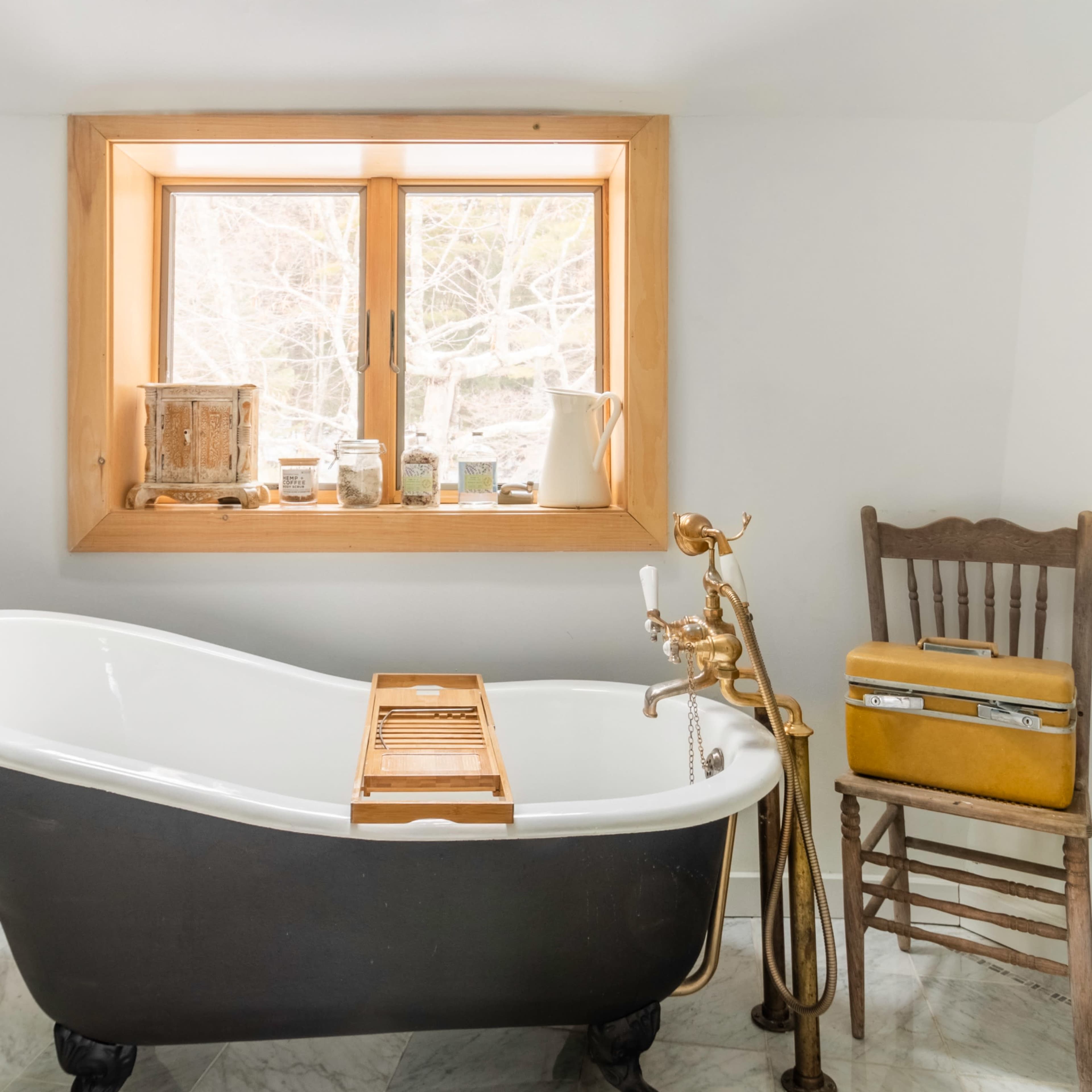 A freestanding bathtub next to a window, accompanied by a wooden chair and a plant in a pot.