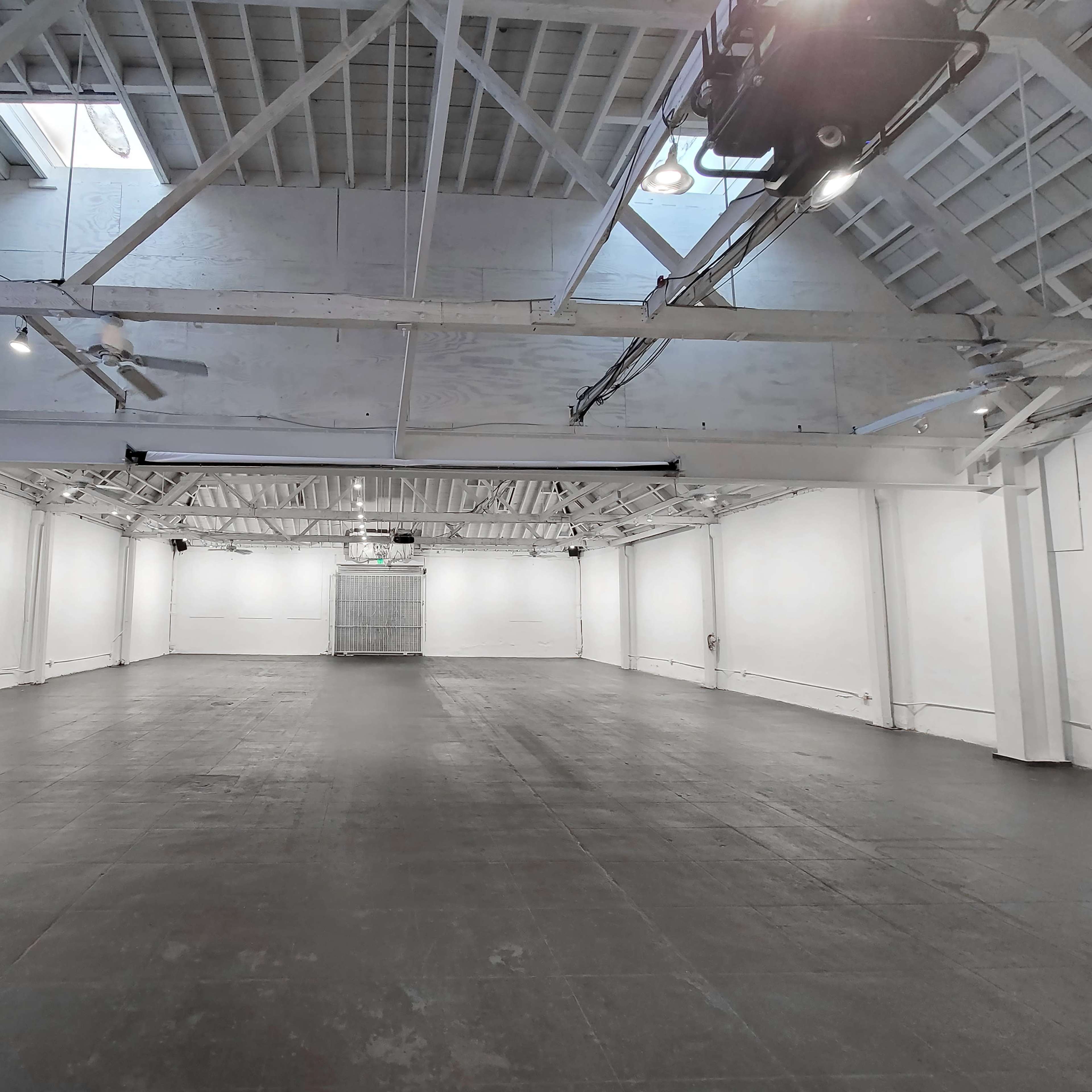 A large, empty industrial space with high ceilings and white walls lit by overhead lights.