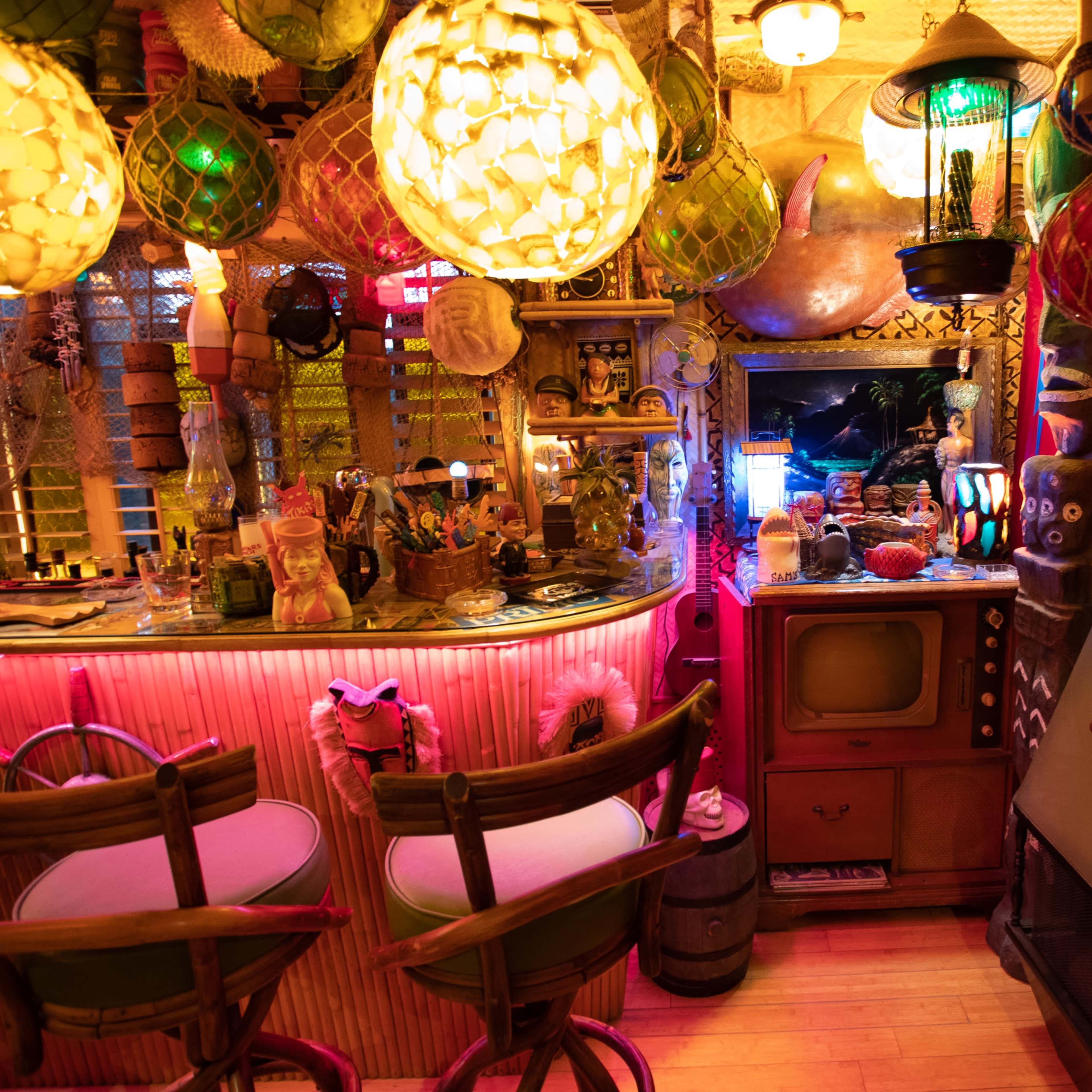 A colorful, eclectic bar area filled with tiki decor, vintage items, and a variety of lighting fixtures.